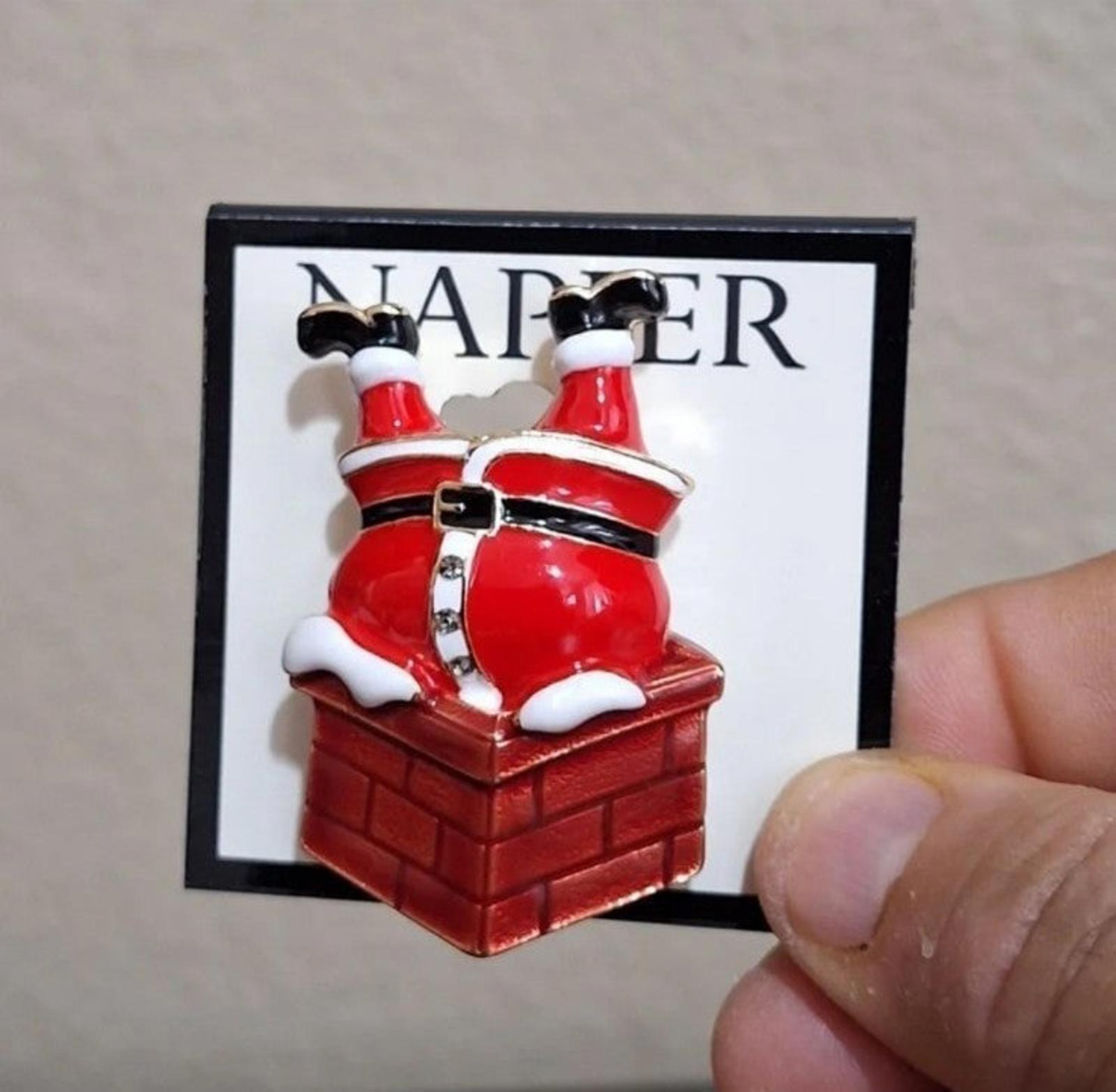 Red enamel Santa climbing down chimney pin on branded card, held by fingertip