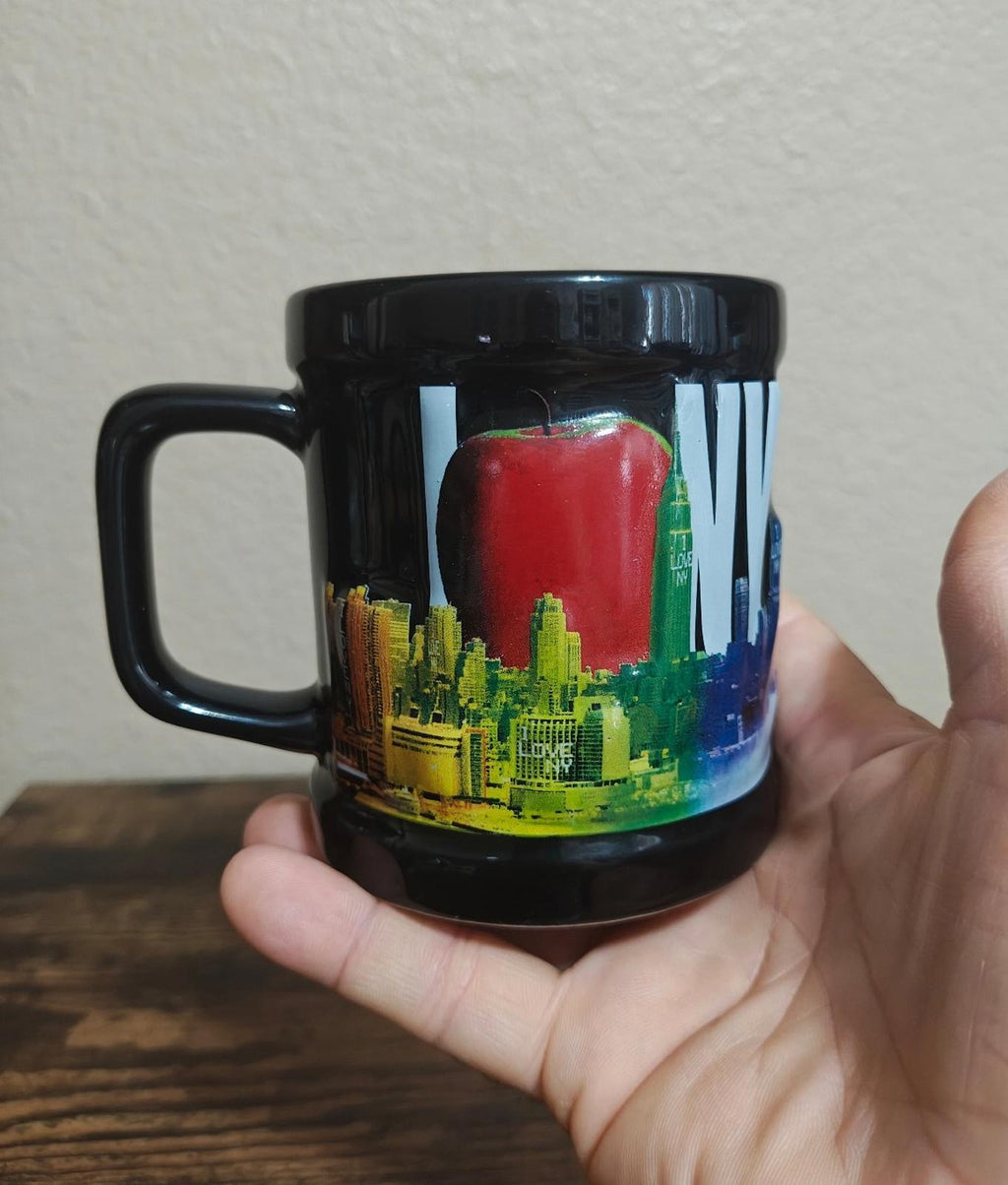 Black ceramic mug with colorful skyline graphic, glossy finish, handle on left