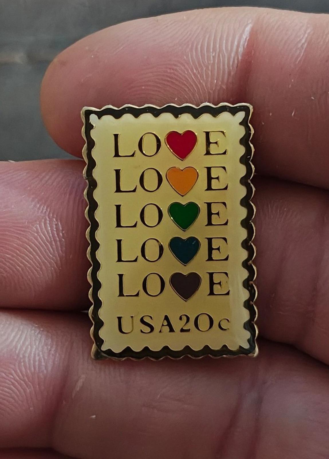 Gold-tone enamel stamp pin with stacked “LOVE” and colored hearts, “USA20c” at bottom.