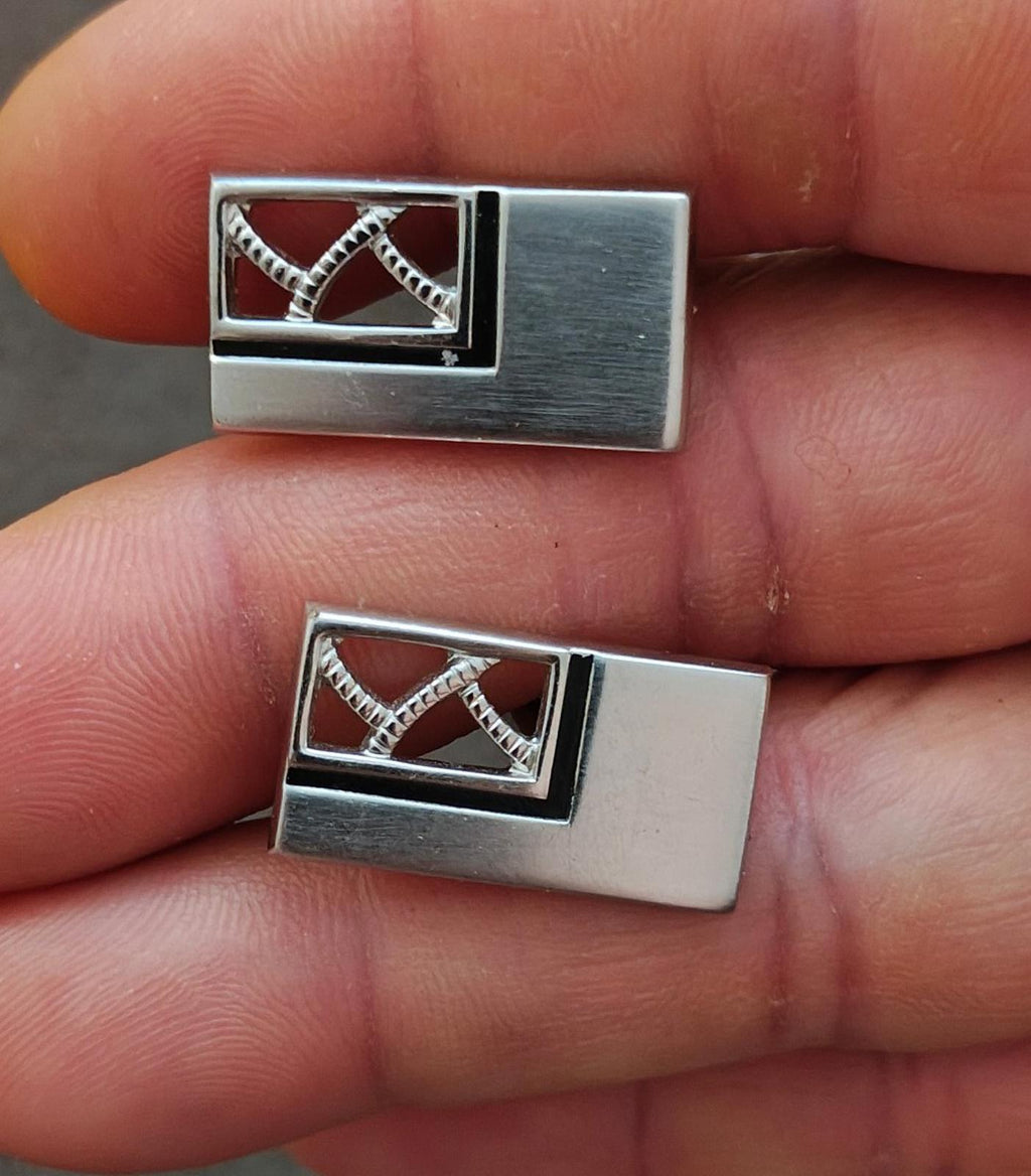 Silver-tone cufflinks close-up showing dark enamel panel with geometric crisscross
