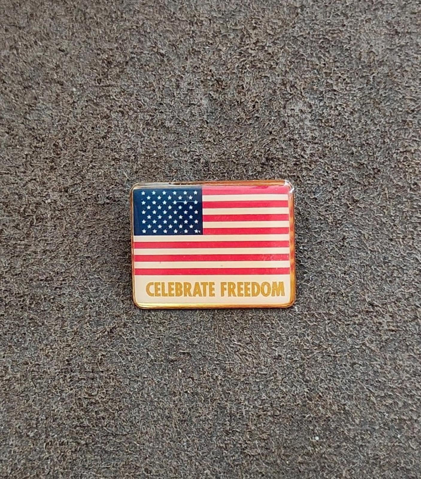 Rectangular gold-tone flag pin reading “CELEBRATE FREEDOM” on the front
