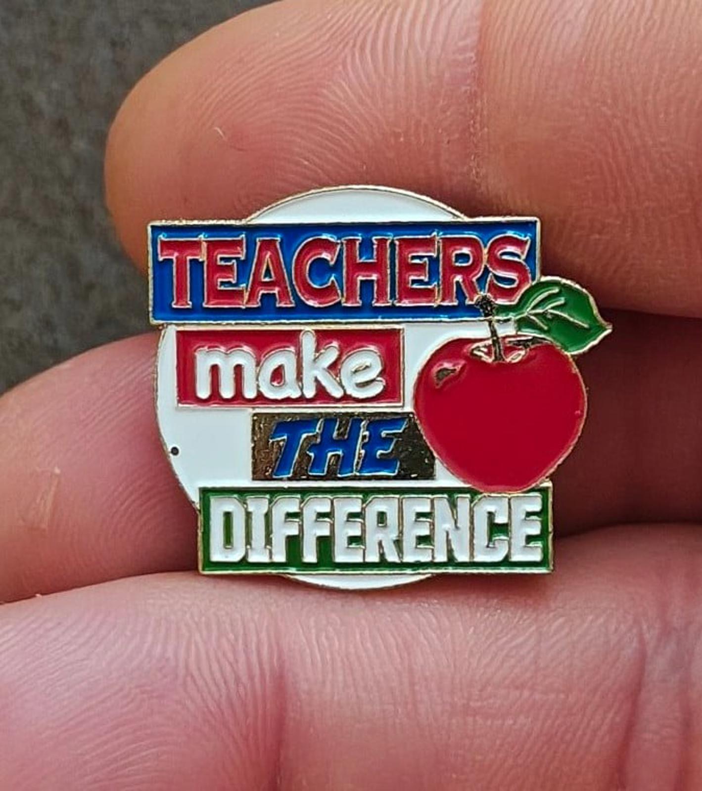 Enamel teacher pin close-up: blue “TEACHERS” and red apple beside slogan