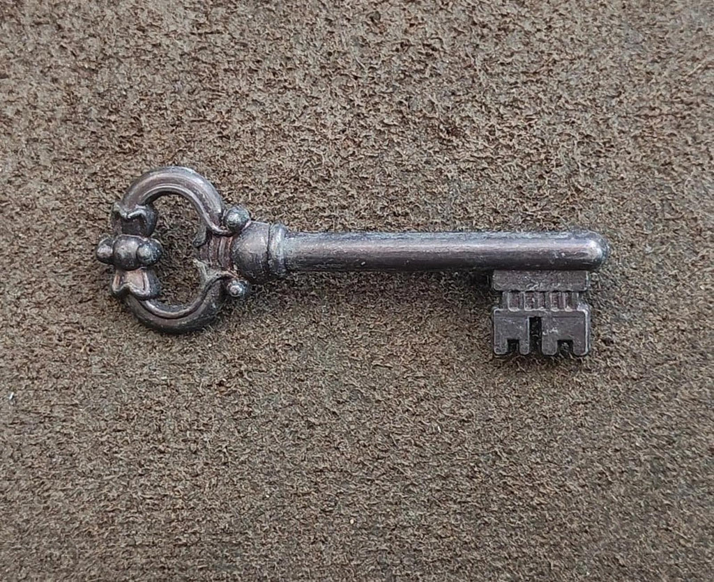 Pewter skeleton key brooch on textured surface, round bow and key head detail