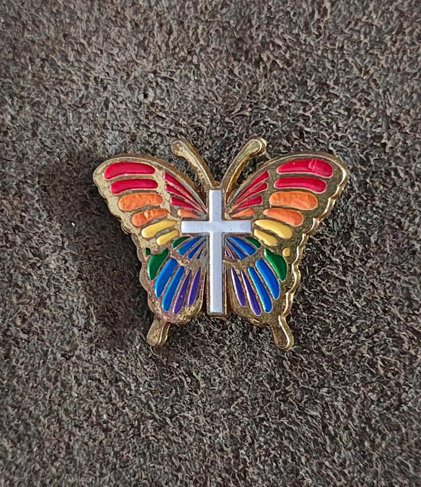 Rainbow butterfly enamel pin with white cross, multicolor wings, gold-tone border
