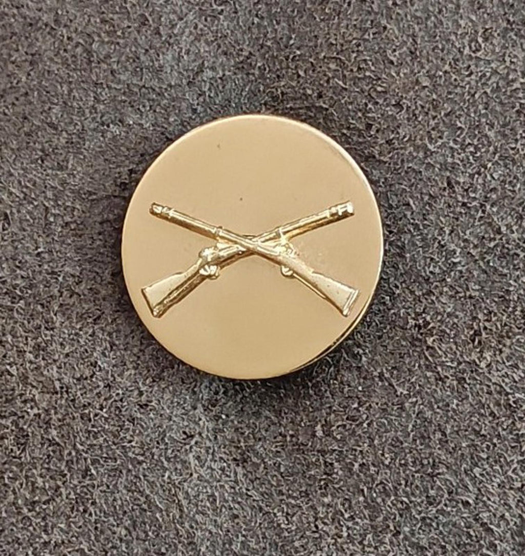 Gold circular brass pin with crossed rifles emblem, centered front