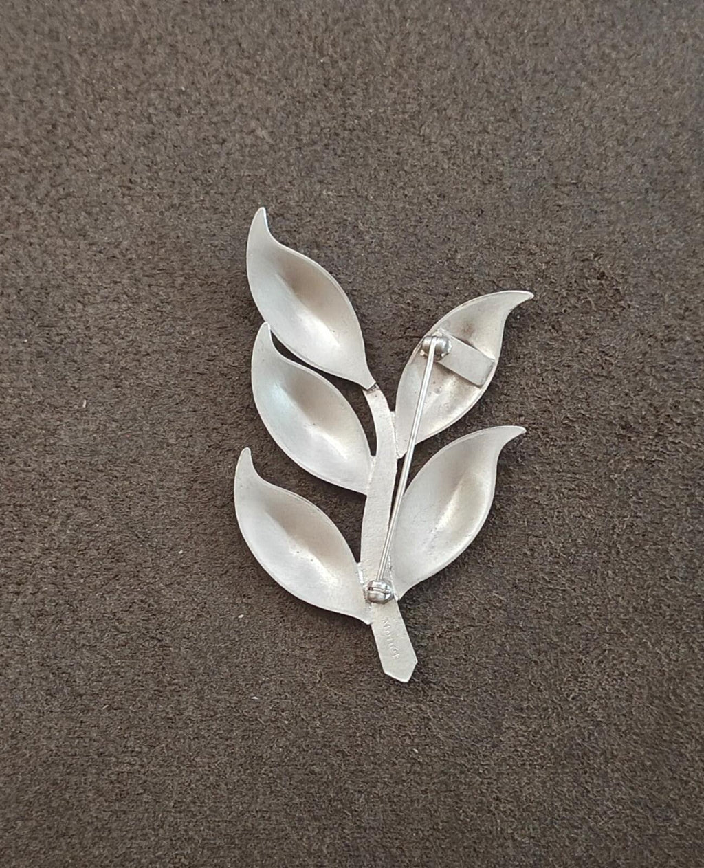 Silver tone modern leaf brooch with five leaves and a small pin clasp at back.