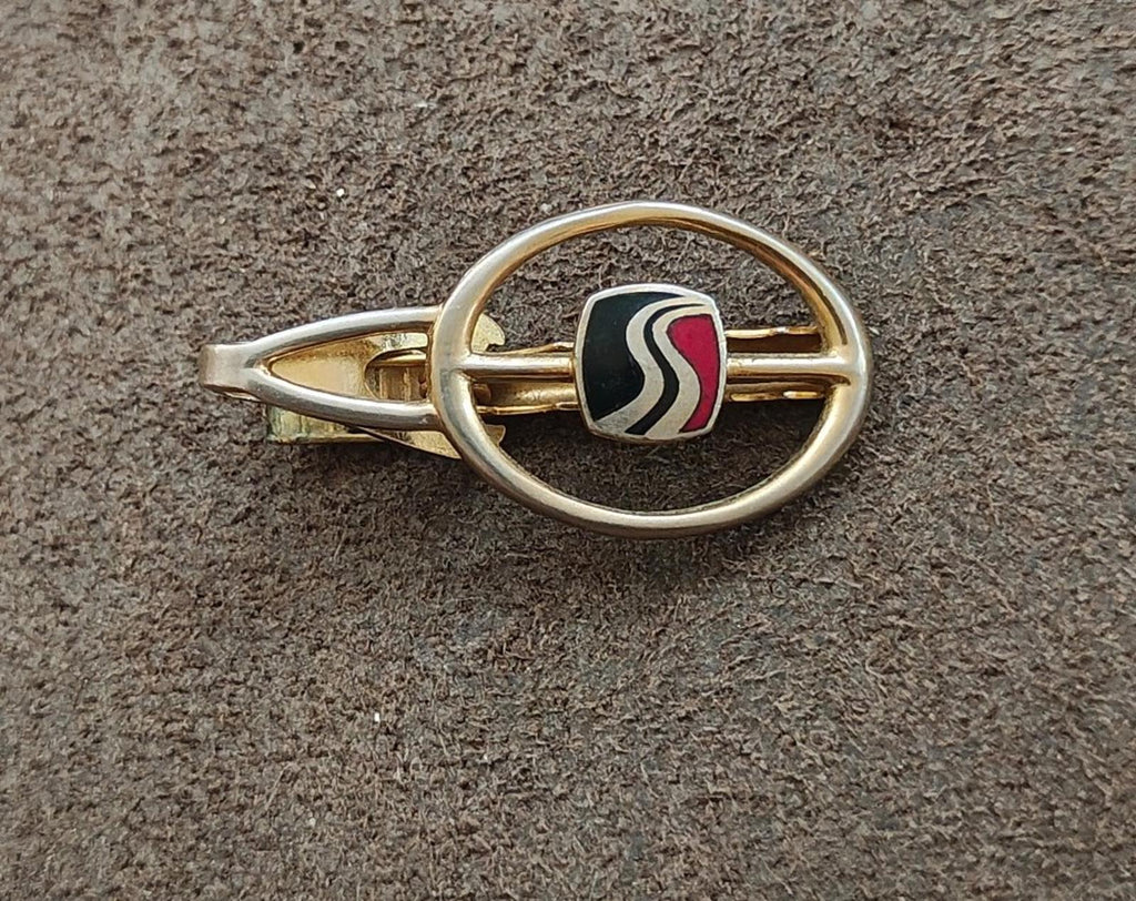 Gold-tone tie clip showing oval ring and black enamel insert with wavy stripe detailing