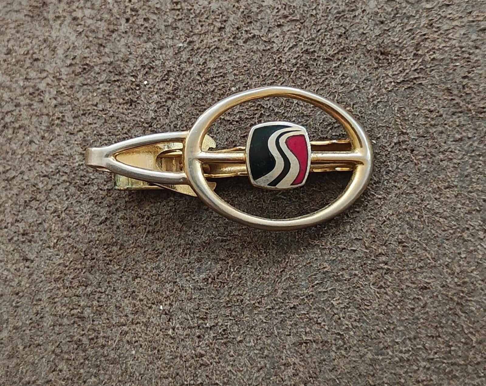 Gold-tone tie clip showing oval ring and black enamel insert with wavy stripe detailing