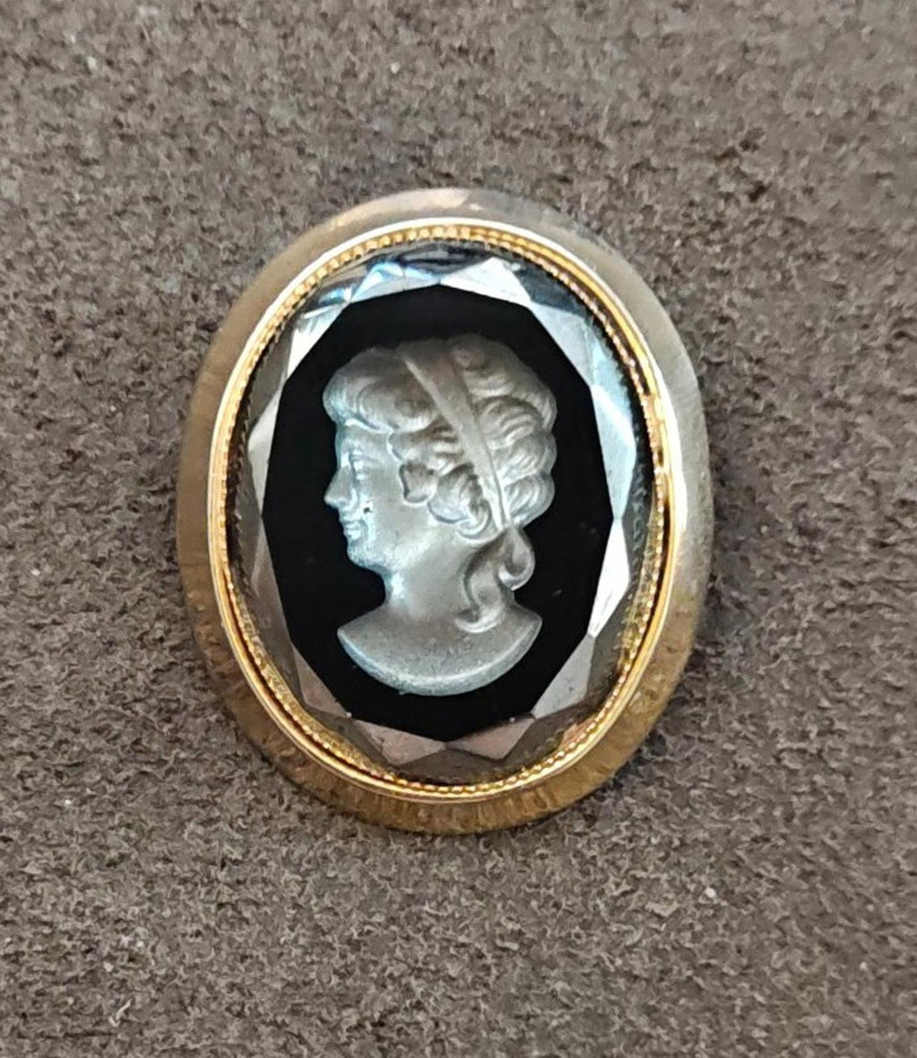 Close view of oval cameo brooch: gold-tone border, black glass, silver profile relief