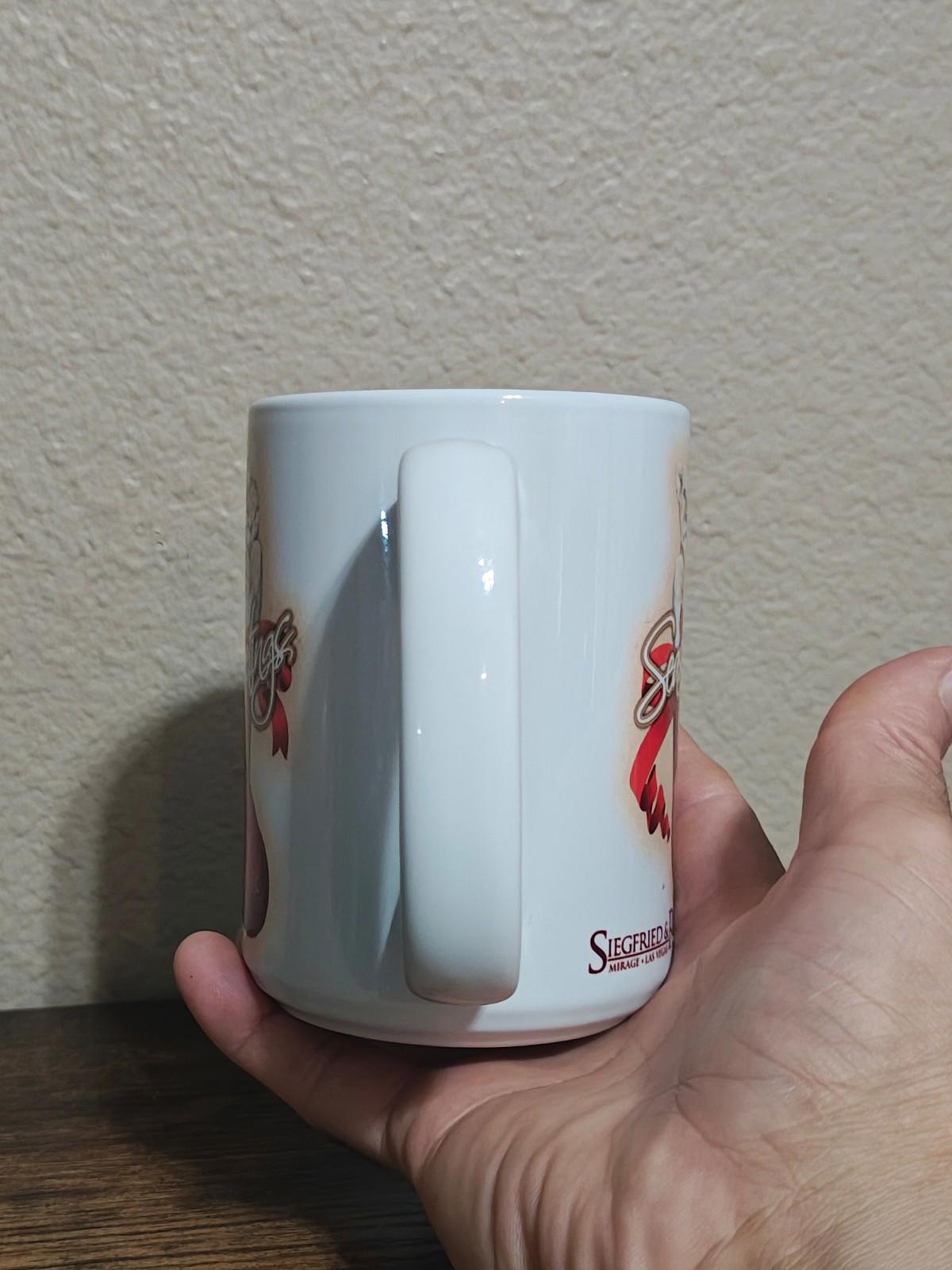 White porcelain mug back view with curved handle and partial “Seasons Greetings” branding