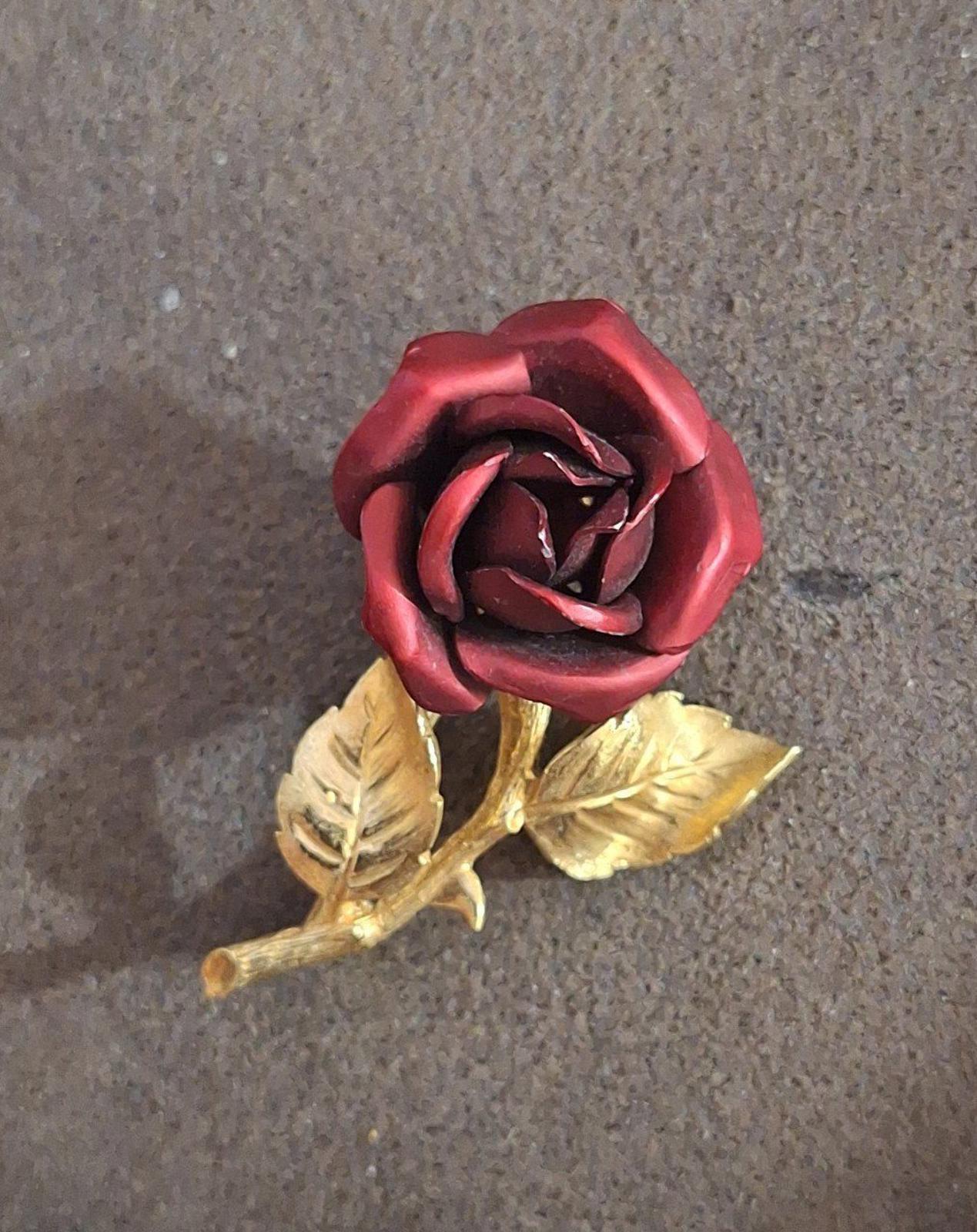 Gold-tone red rose enamel pin brooch with raised leaves and stem, angled view.