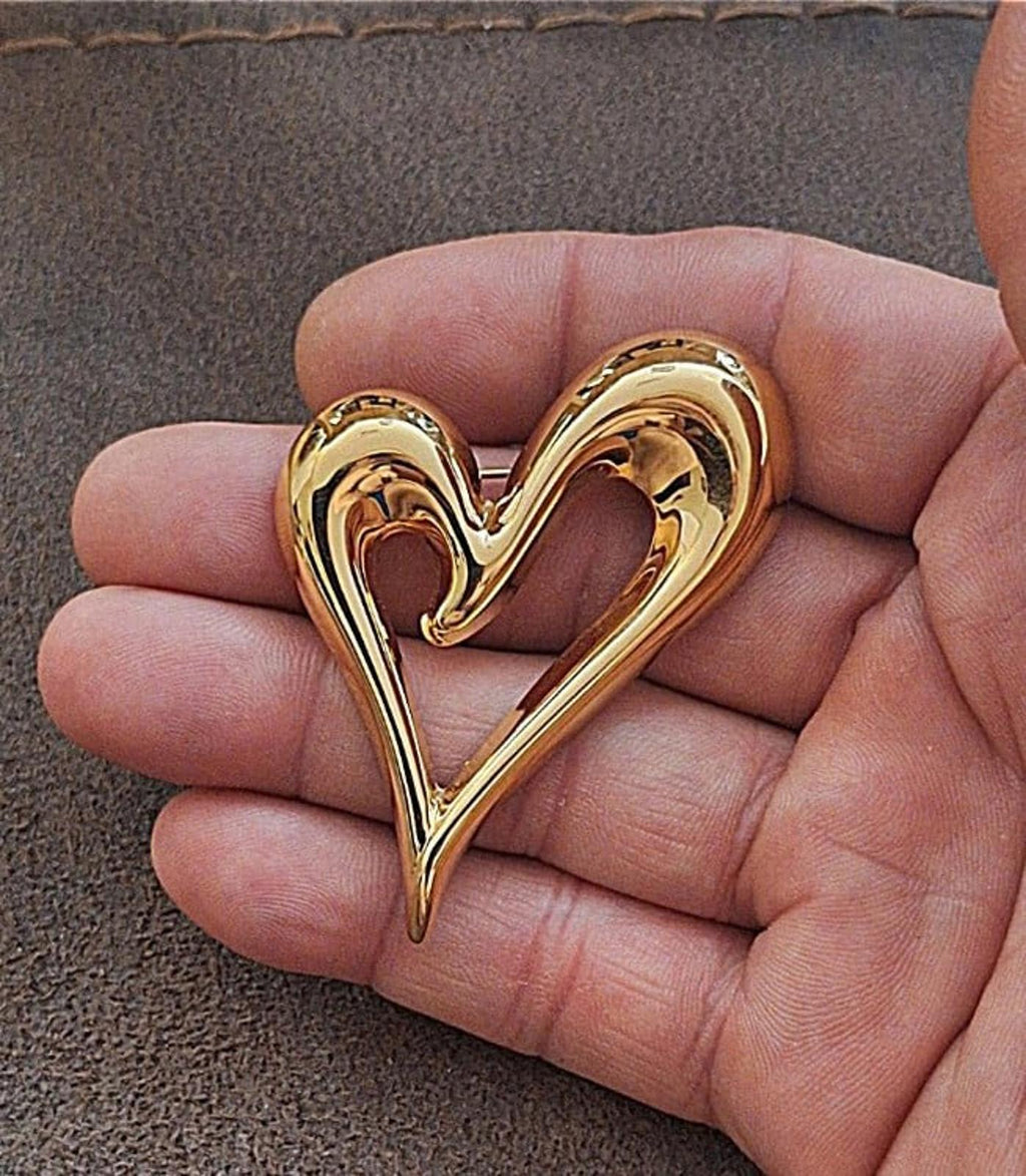 Gold heart pin with open center, held in hand, glossy raised heart outline