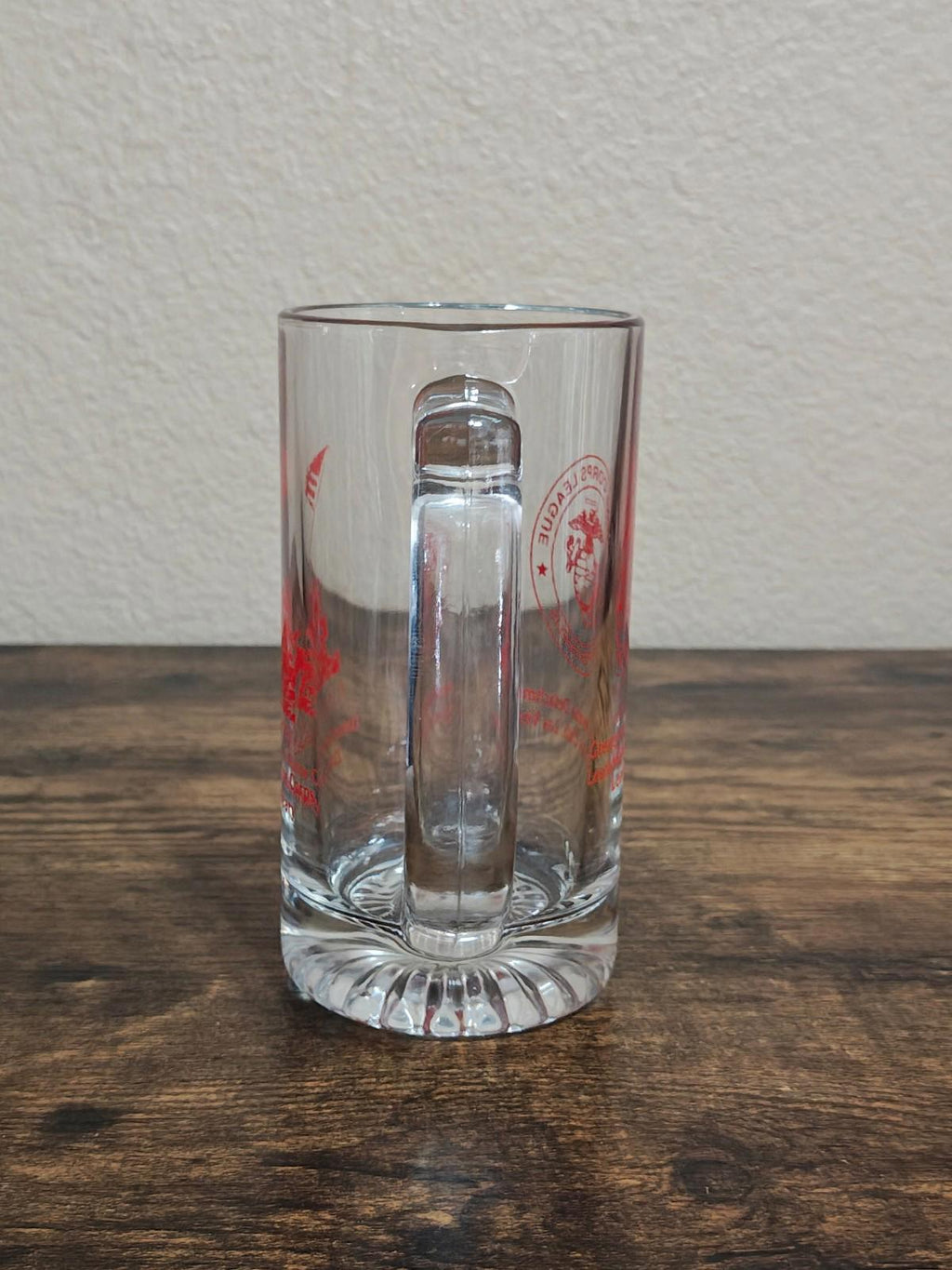 Clear glass beer mug standing on table, red logo visible near the top