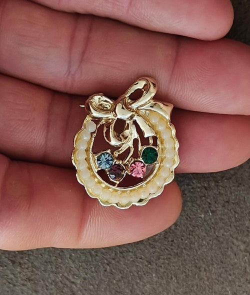 Gold-tone wreath brooch with cream faux pearl edge and colorful rhinestone centerpiece.