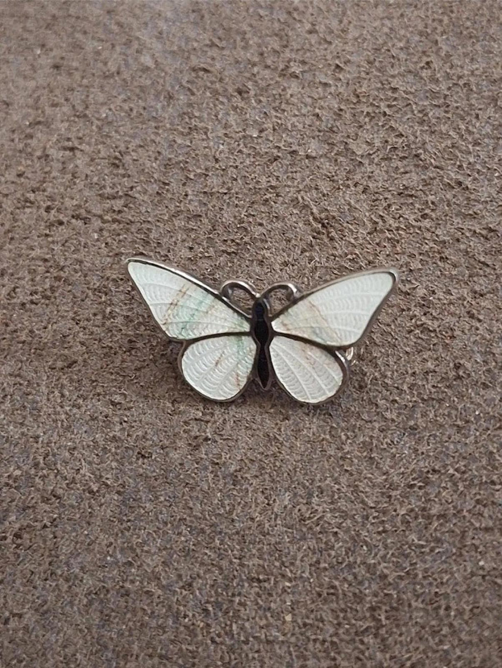 Enamel butterfly pin brooch with white wings and dark body, centered on fabric.