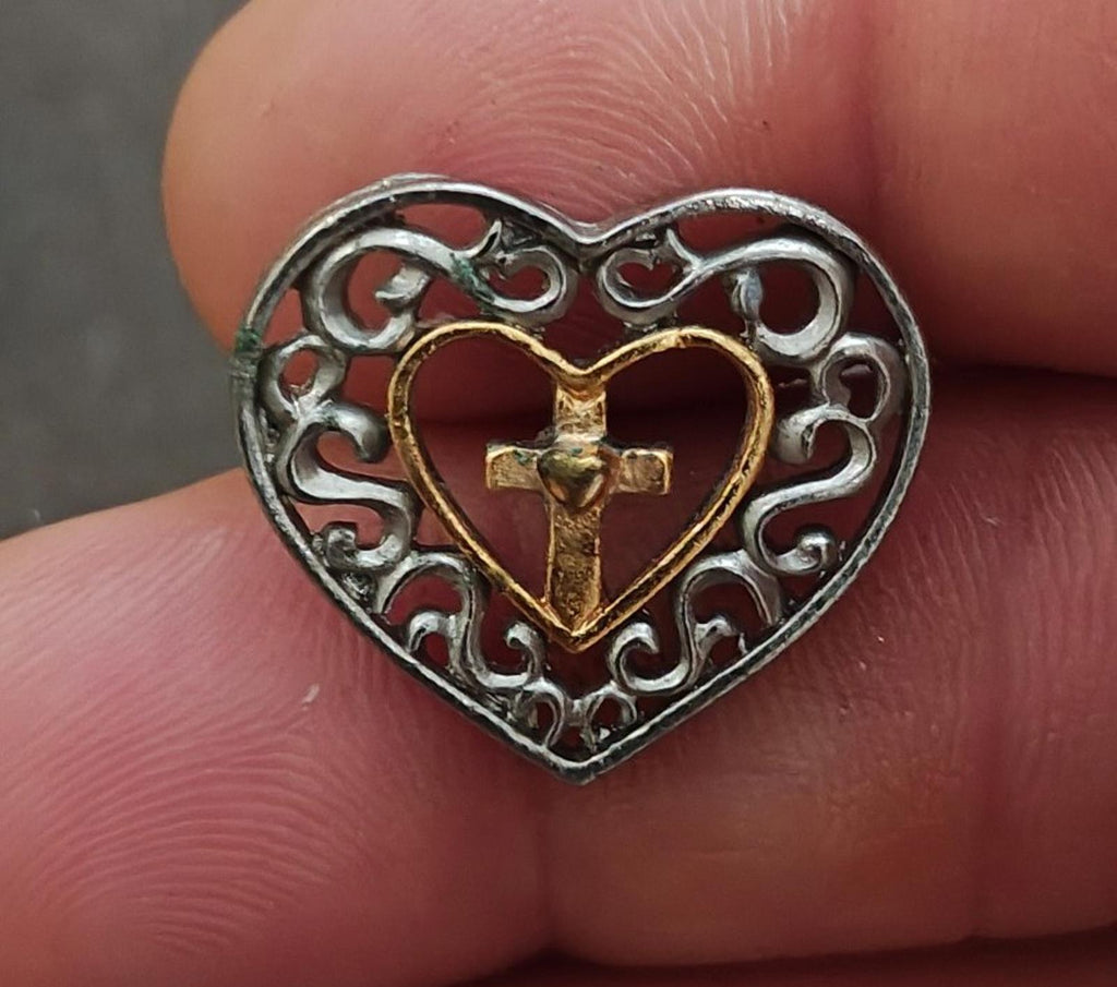 Heart cross pin close-up on fingertip; silver filigree with gold-toned heart and cross
