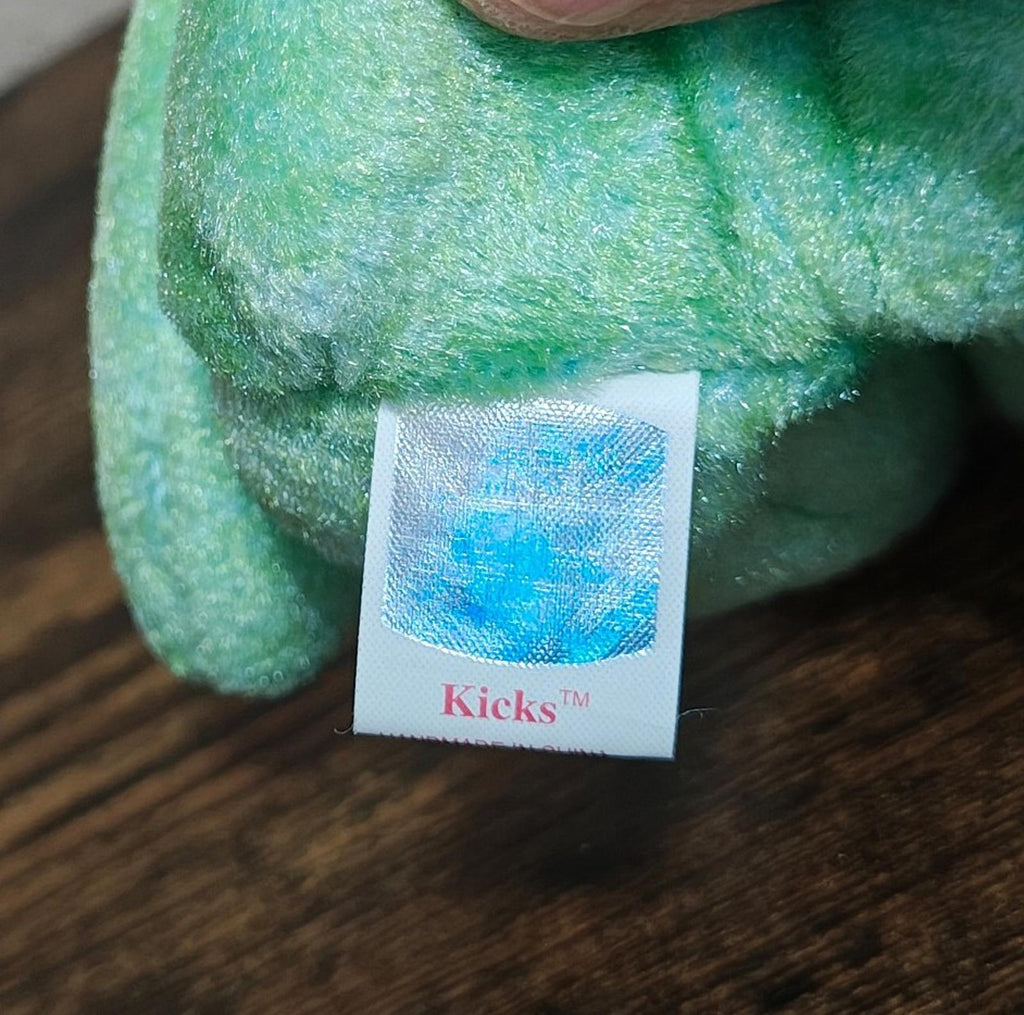 White square label reading Kicks on green teddy bear plush.