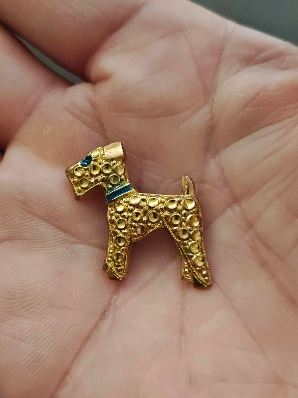 Gold-tone terrier dog brooch with blue enamel accents and detailed filigree circles.