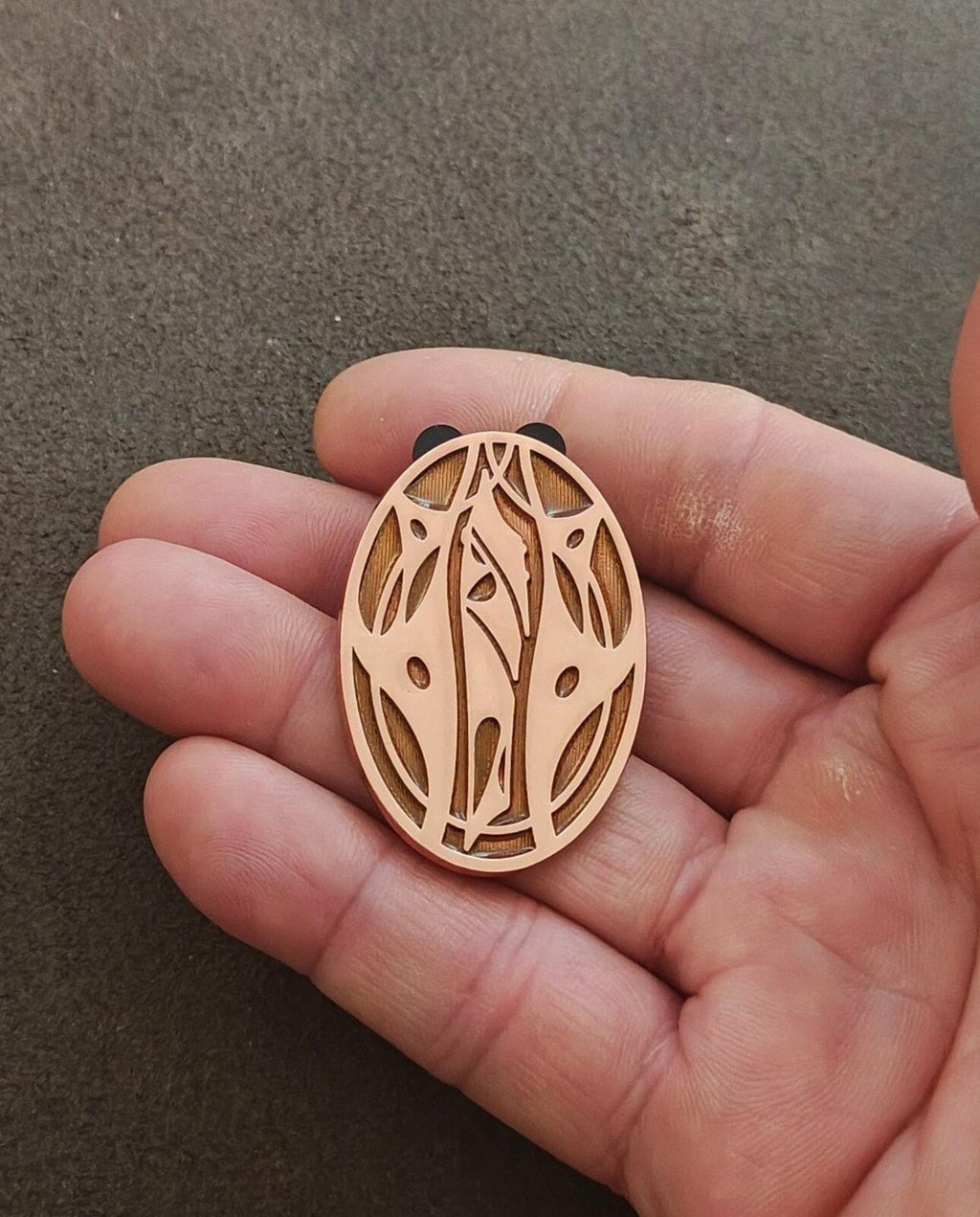 Apricot oval enamel pin with leaf-and-vine cutouts shown in hand