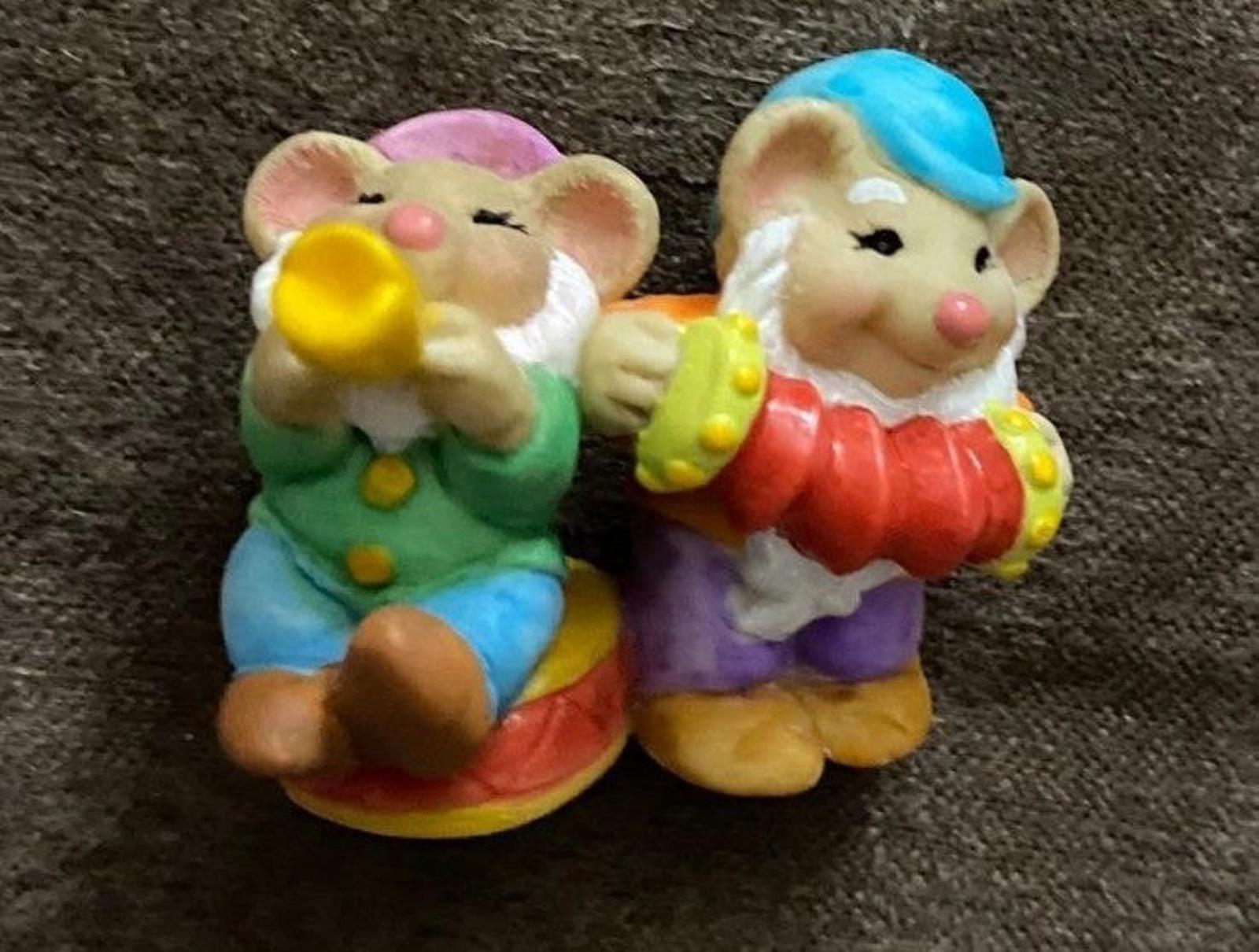 Two dwarf figurines in green and purple outfits, smiling and holding a yellow accessory.