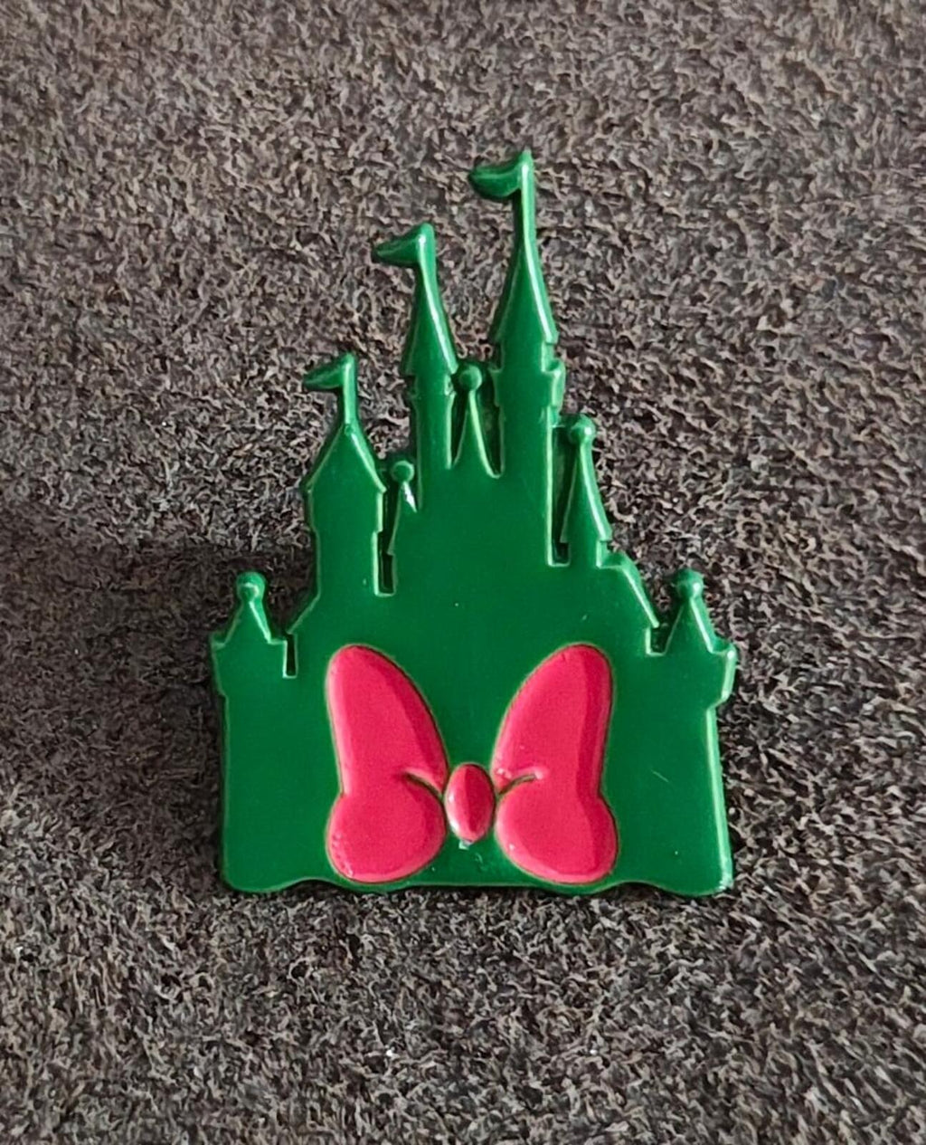 Green castle enamel pin with pink bow and spires on textured surface