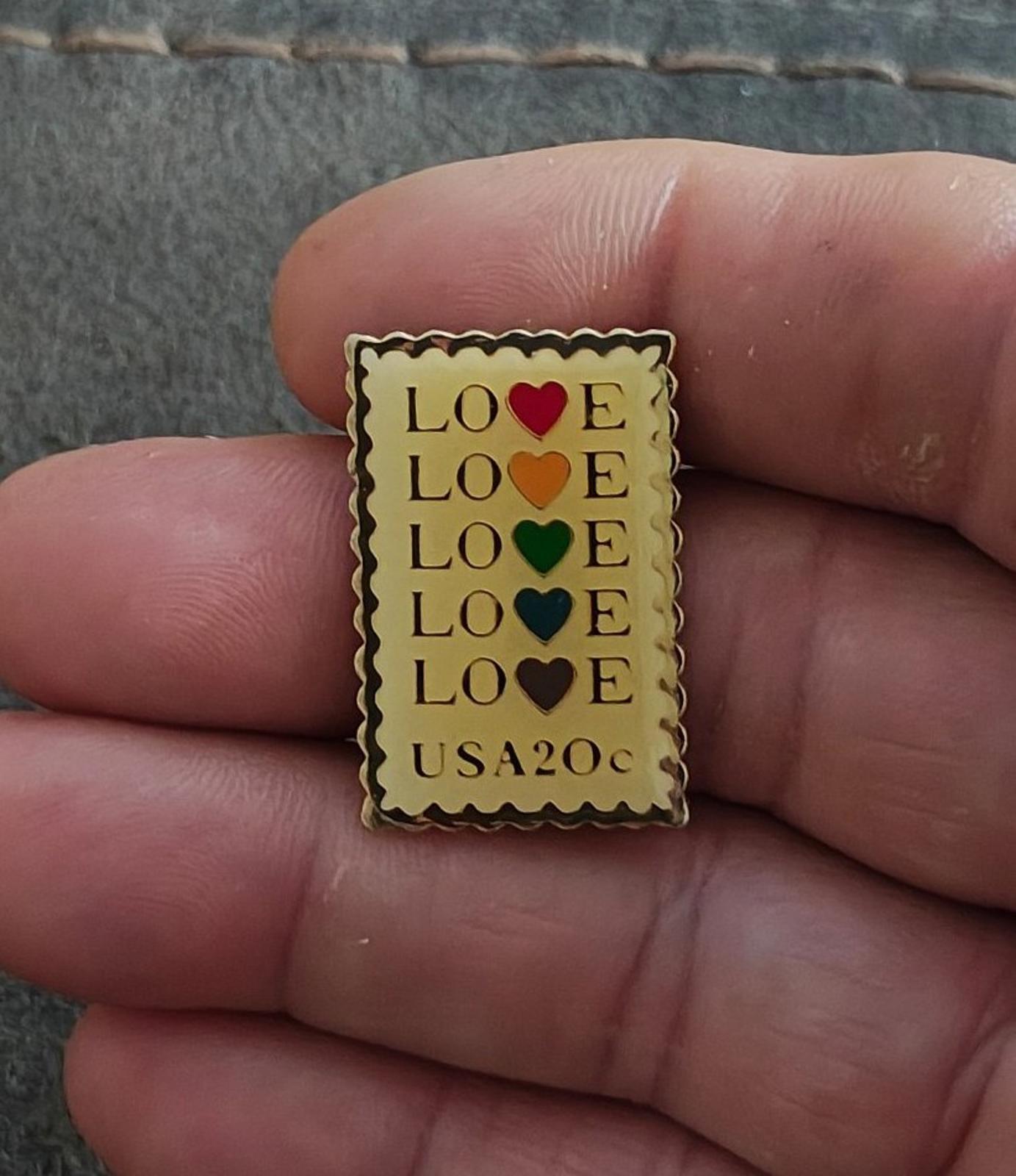 Gold-tone enamel USPS-style pin with “LOVE” rows and small “USA20c” near the bottom edge.