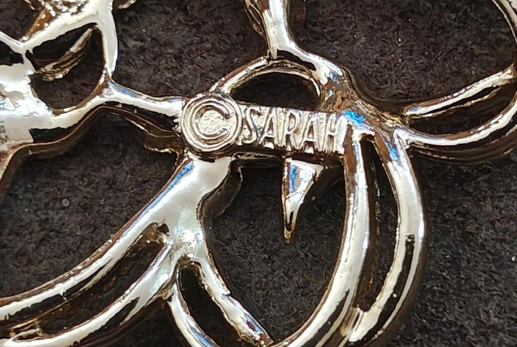 Gold-tone brooch close-up with engraved name “SARAH” on the metal