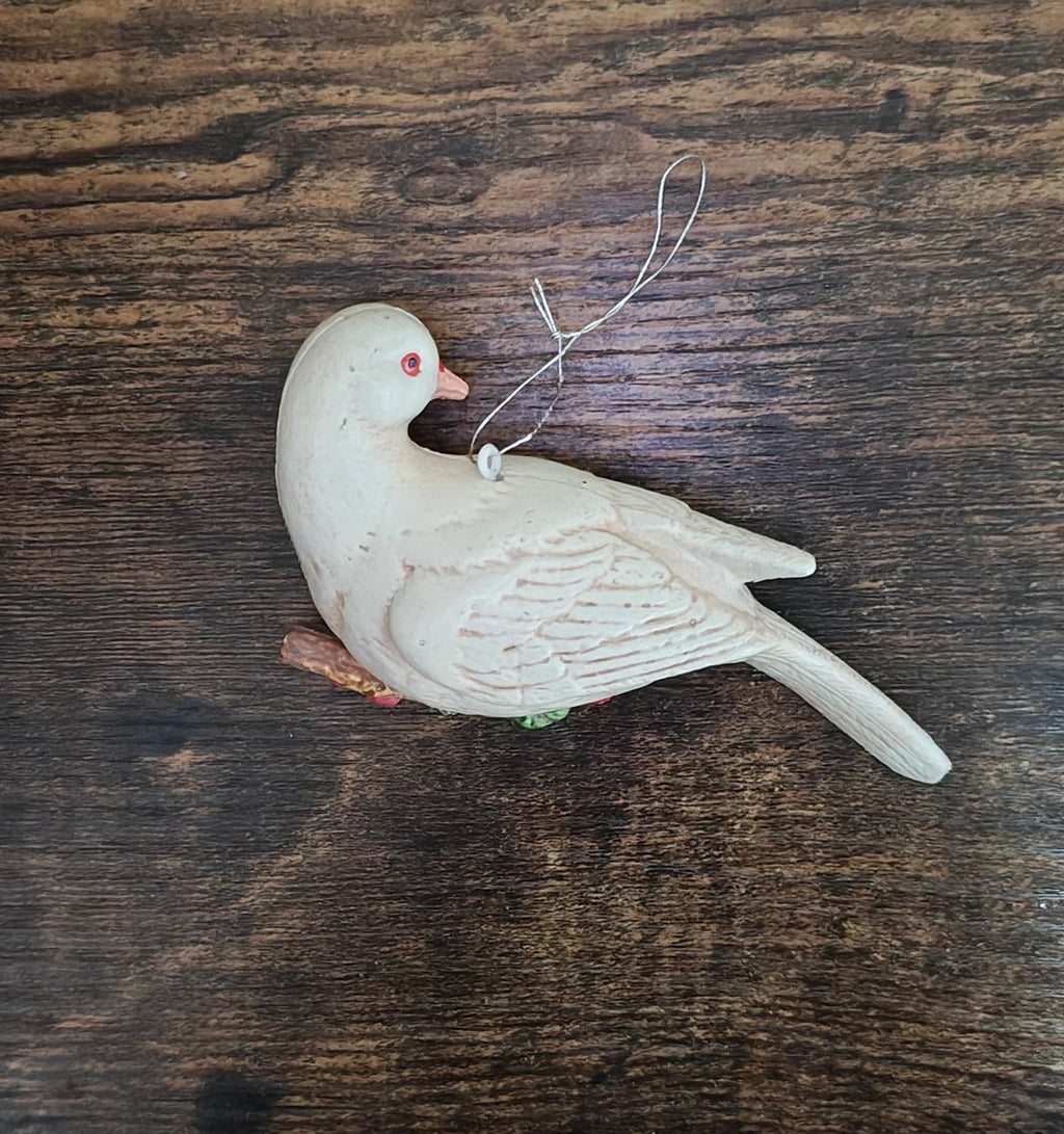 White plastic dove ornament on wood with red eye, green scarf, and two hanging loops.