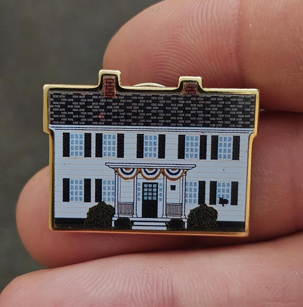 White enamel building scene pin with black trees and gold border, front view