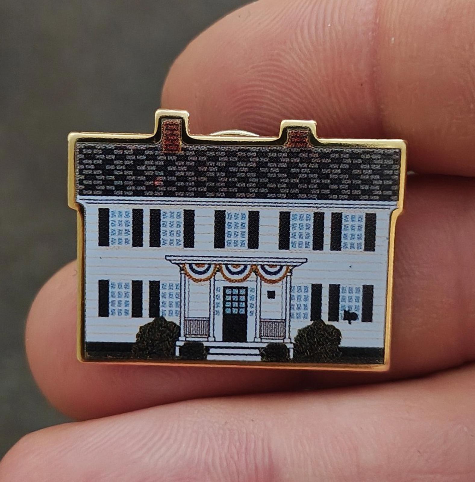 White enamel building scene pin with black trees and gold border, front view