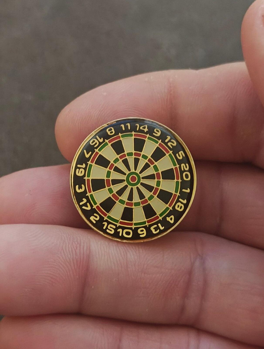 Gold-tone dartboard enamel pin close-up, green and red segment spokes with black numbering ring.