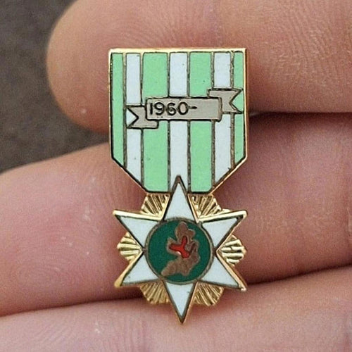 Green-and-white striped enamel campaign pin with central red emblem on star.