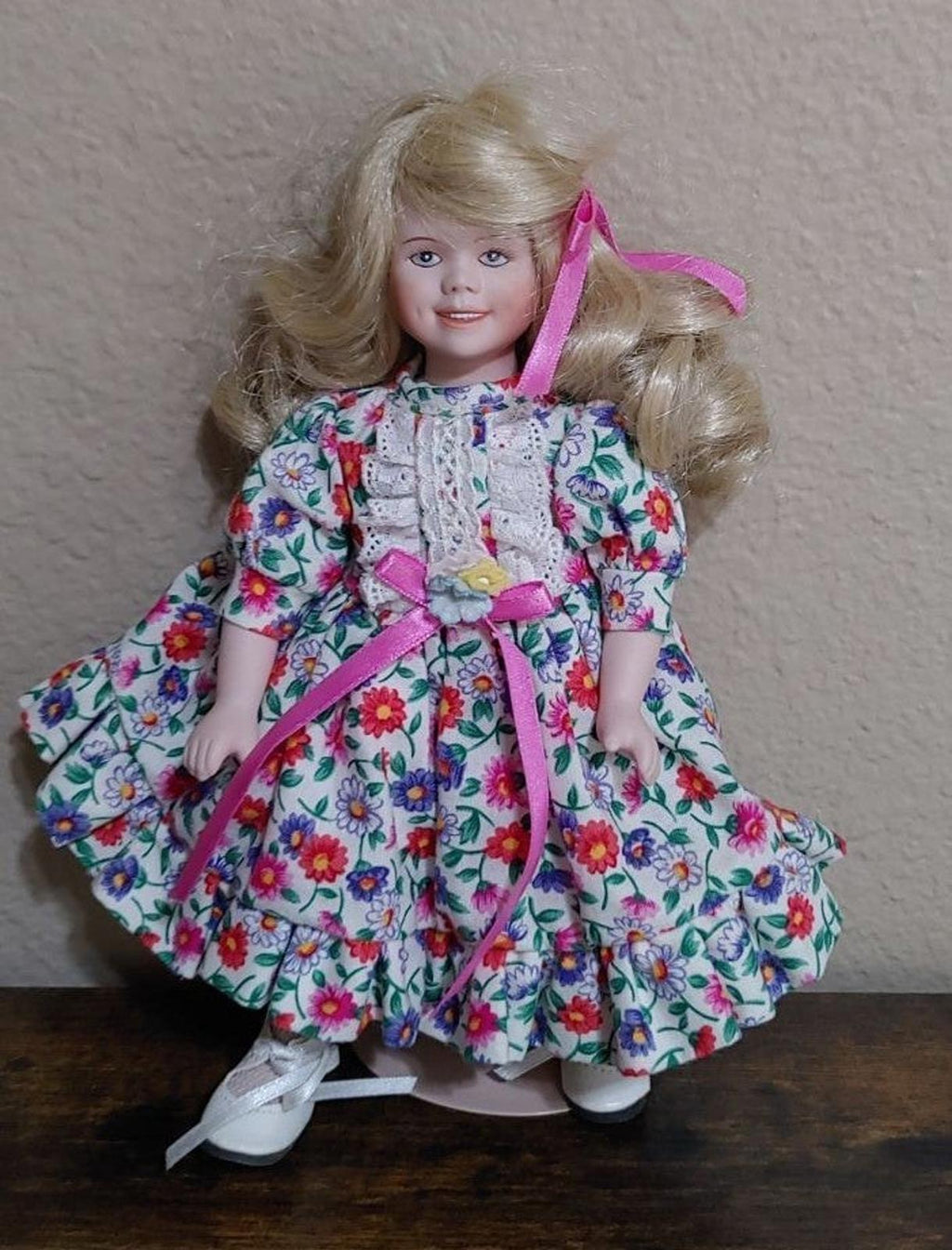 Porcelain doll front view with blonde hair curls, pink ribbons, and floral skirt