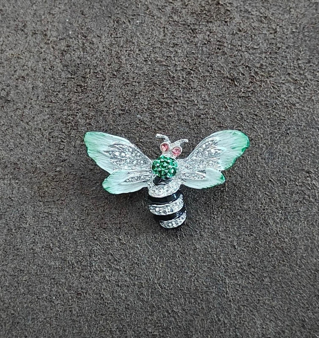 Bee enamel brooch on gray surface: mint green wings, green center, pink rhinestone eyes