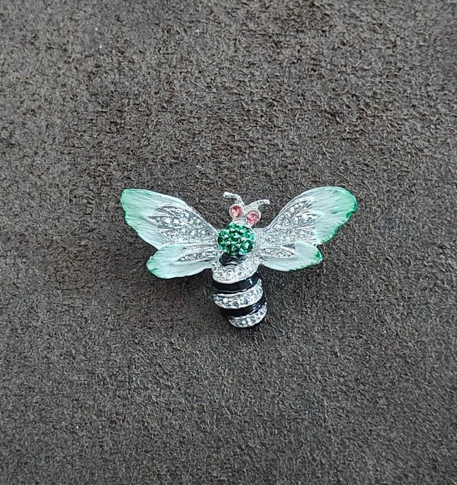 Bee enamel brooch on gray surface: mint green wings, green center, pink rhinestone eyes