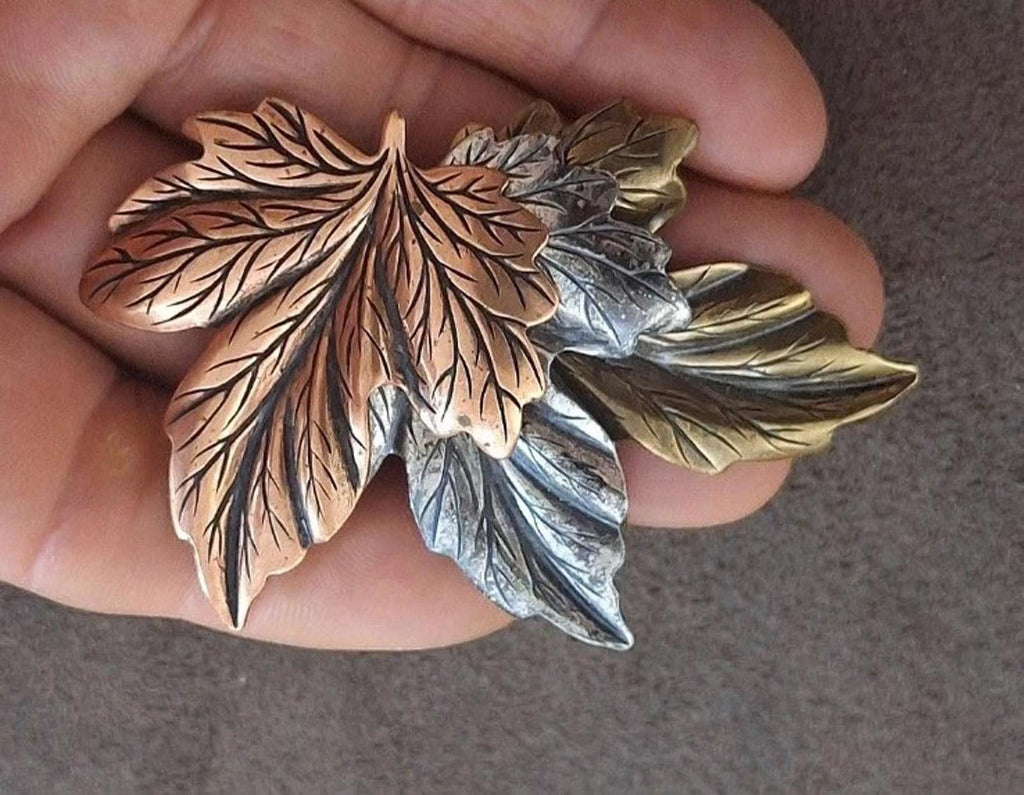 Layered leaf pin brooch with brown, gold, and silver leaves, held in hand