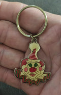 Gold-tone ring keychain with colorful clown face charm, held in a hand