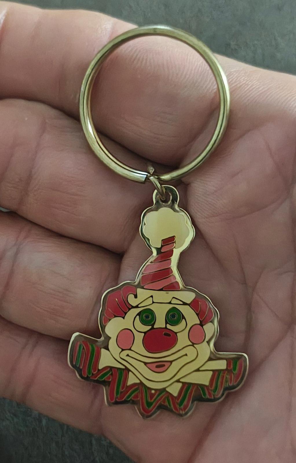 Gold-tone ring keychain with colorful clown face charm, held in a hand