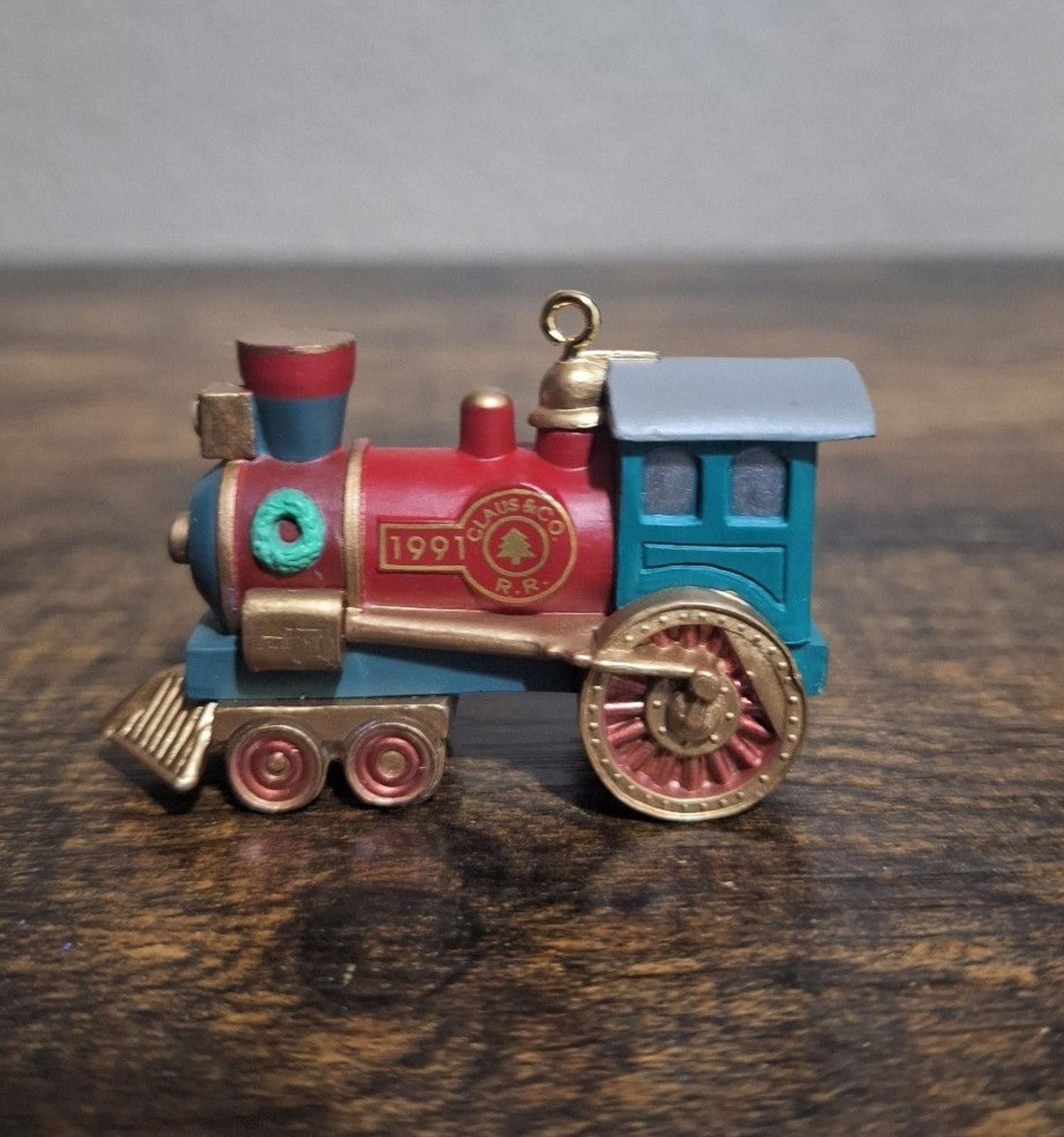 Blue and red train locomotive ornament on base, front view with gold bell and hanging loop