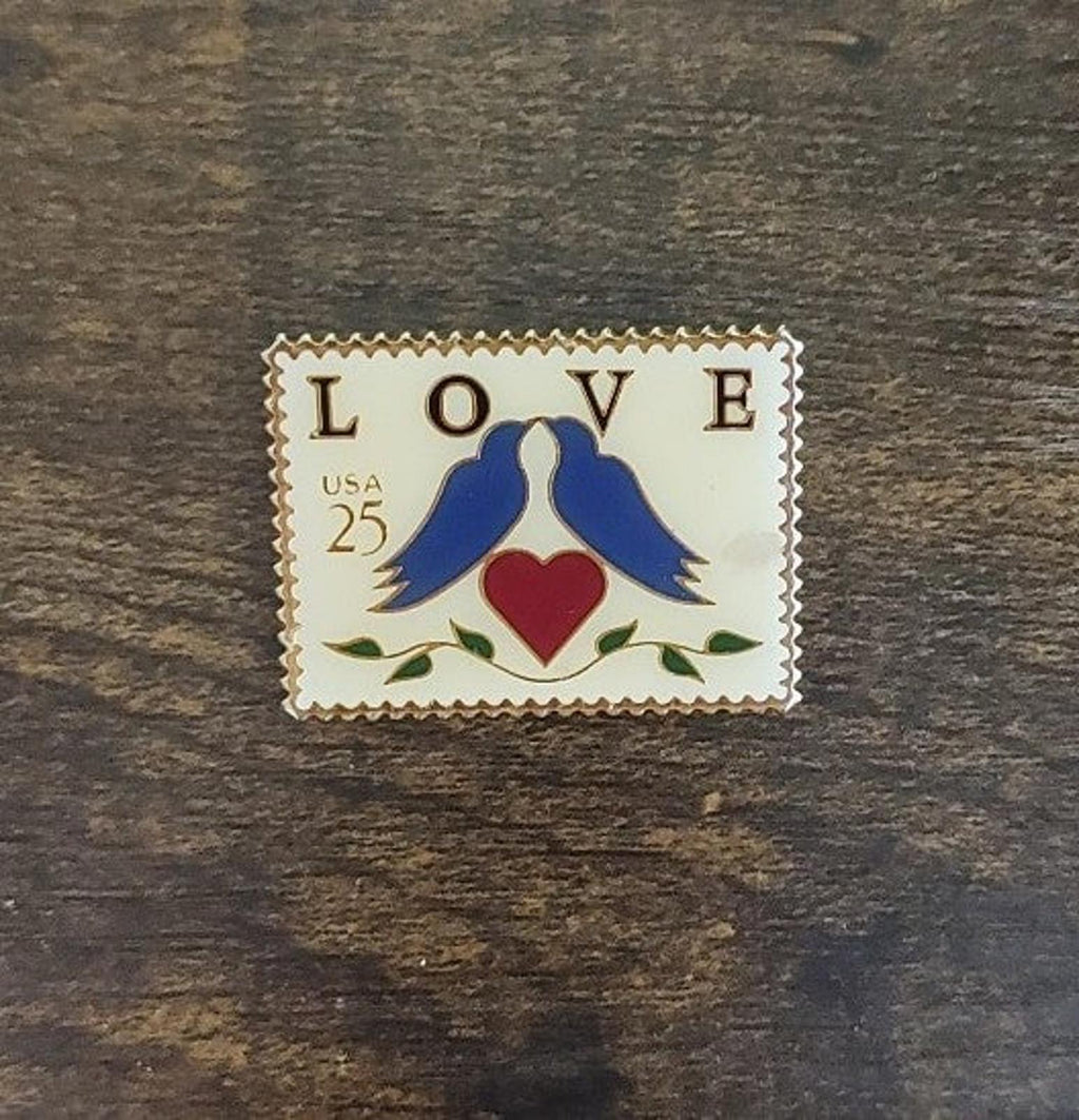 Blue lovebirds enamel pin with red heart below “LOVE”, “USA 25” stamp text