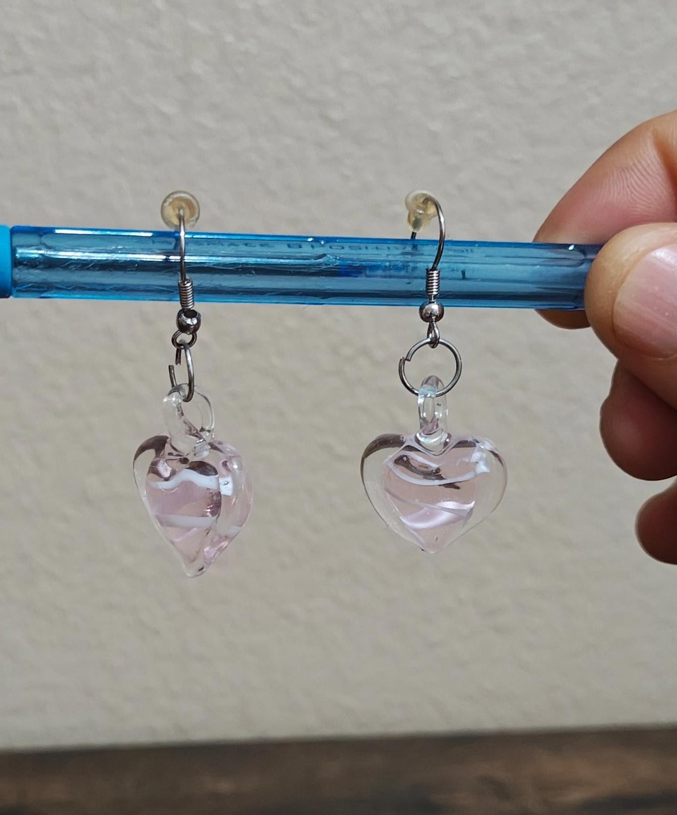 Heart-shaped glass earrings with swirl detail; one heart shows a faint pink tint.