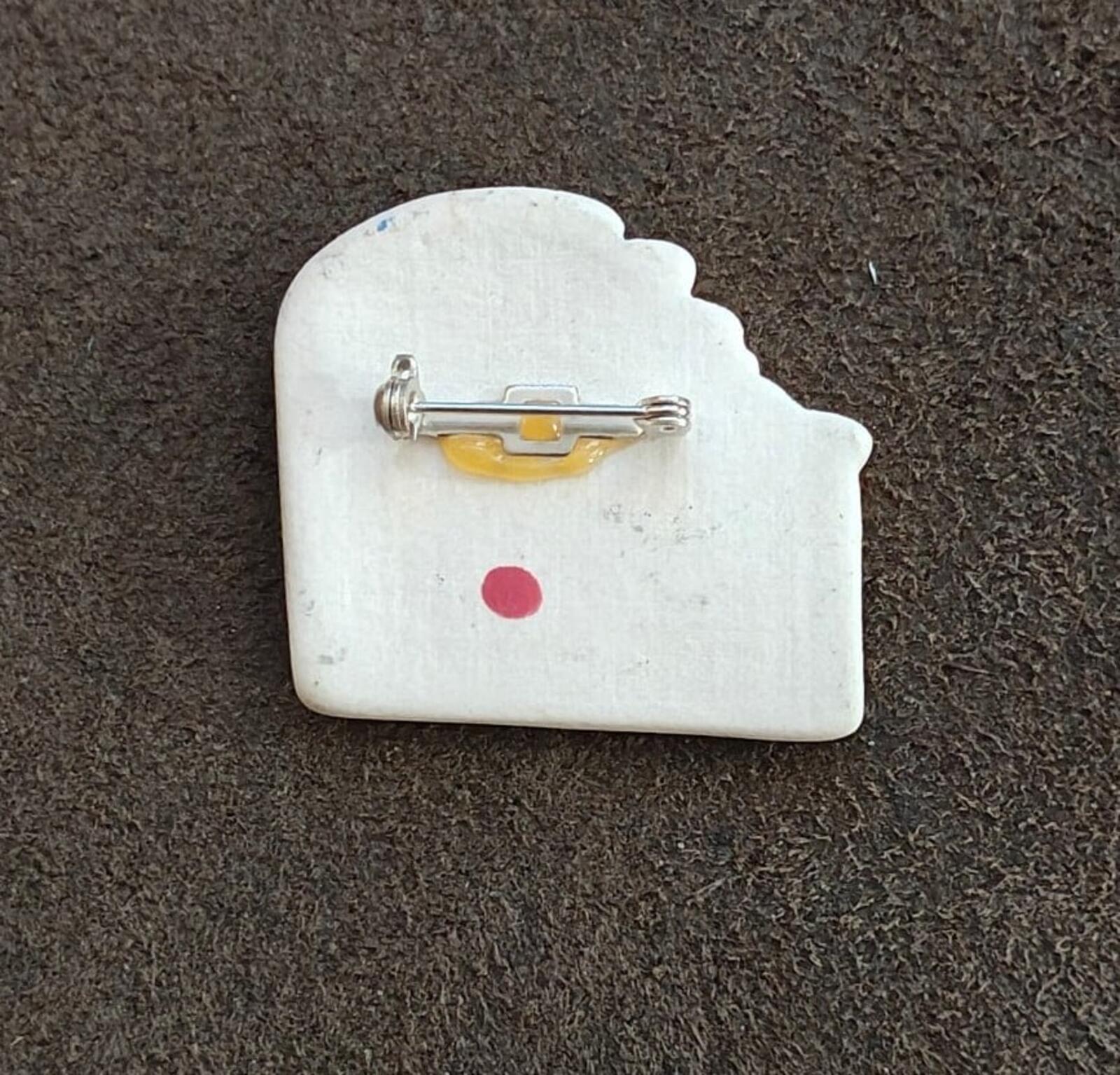 Back of enamel angel brooch with metal pin and clasp, small red dot detail