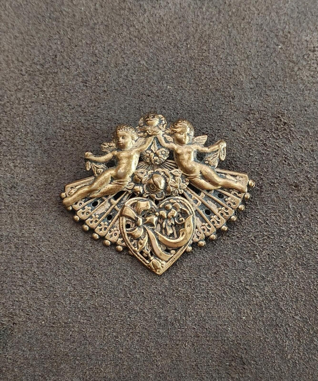 Gold-tone cherub brooch lying flat, diamond frame with detailed filigree