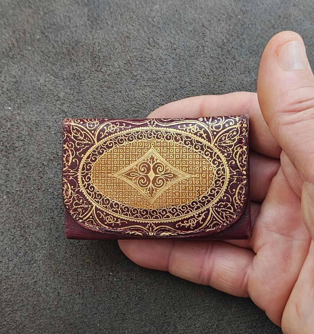 Small coin purse wallet, burgundy leather with gold ornamental embossed oval front design.
