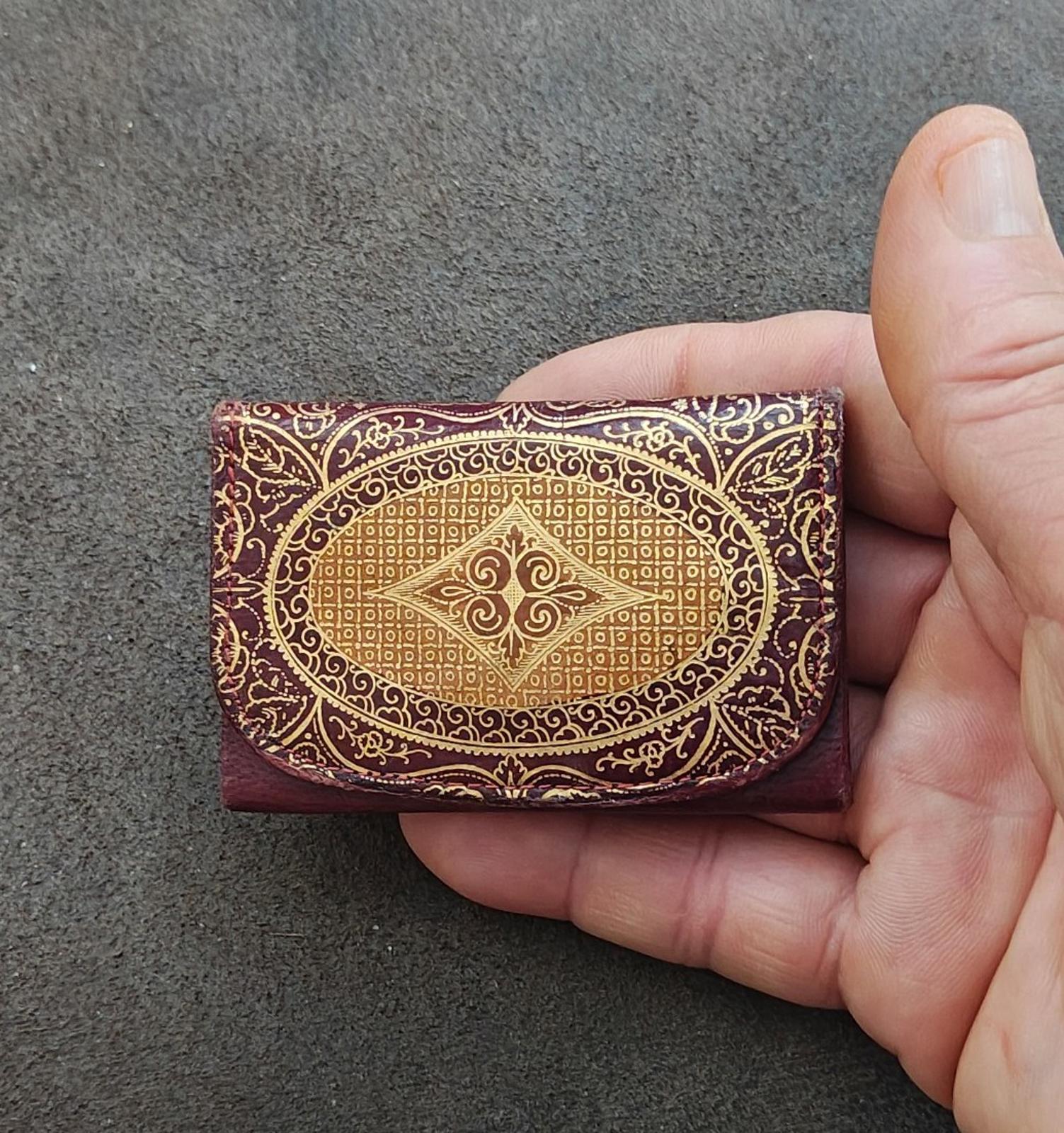 Small coin purse wallet, burgundy leather with gold ornamental embossed oval front design.