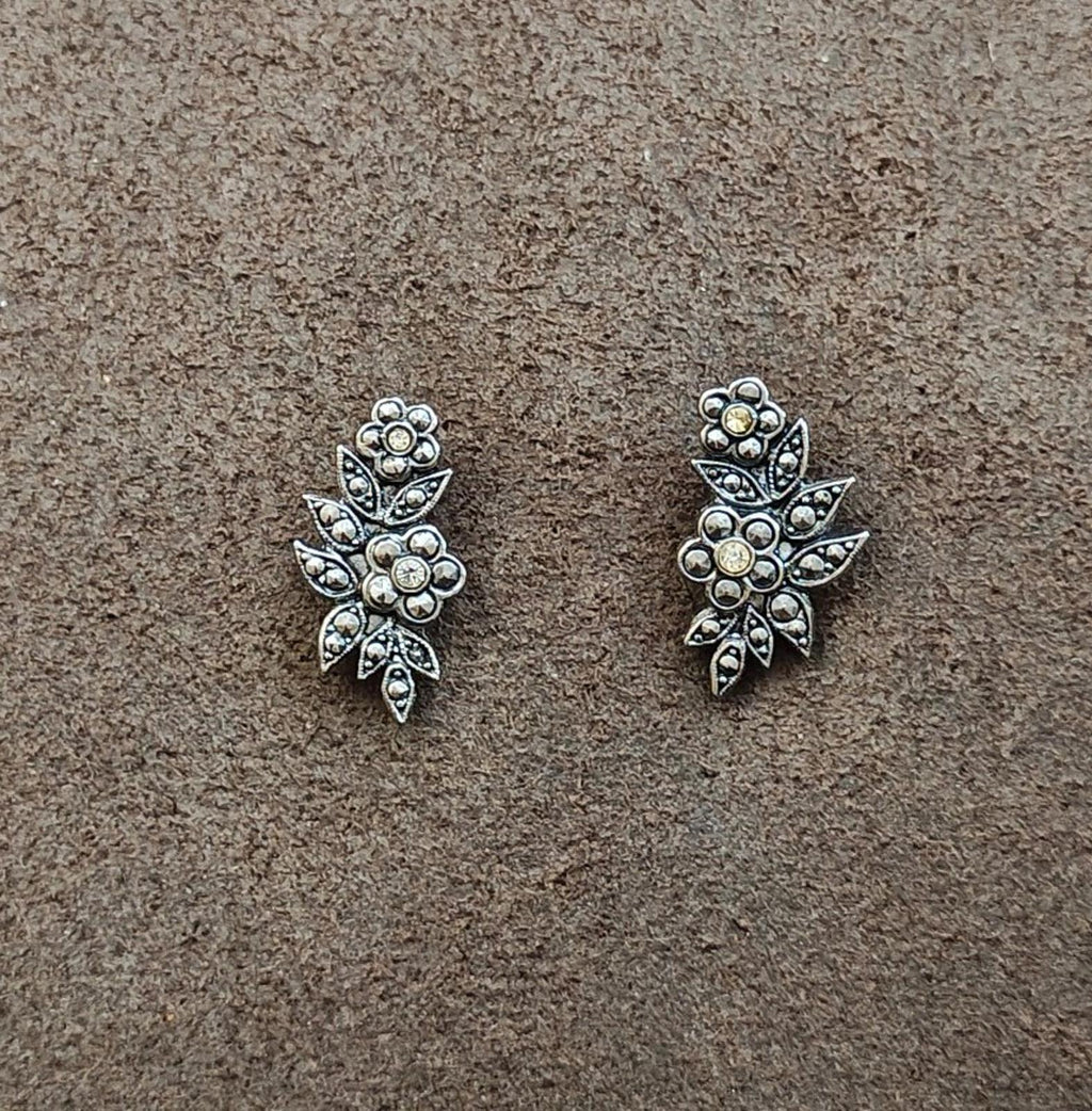 Silver tone floral leaf stud earrings with round rhinestones in an ornate starburst