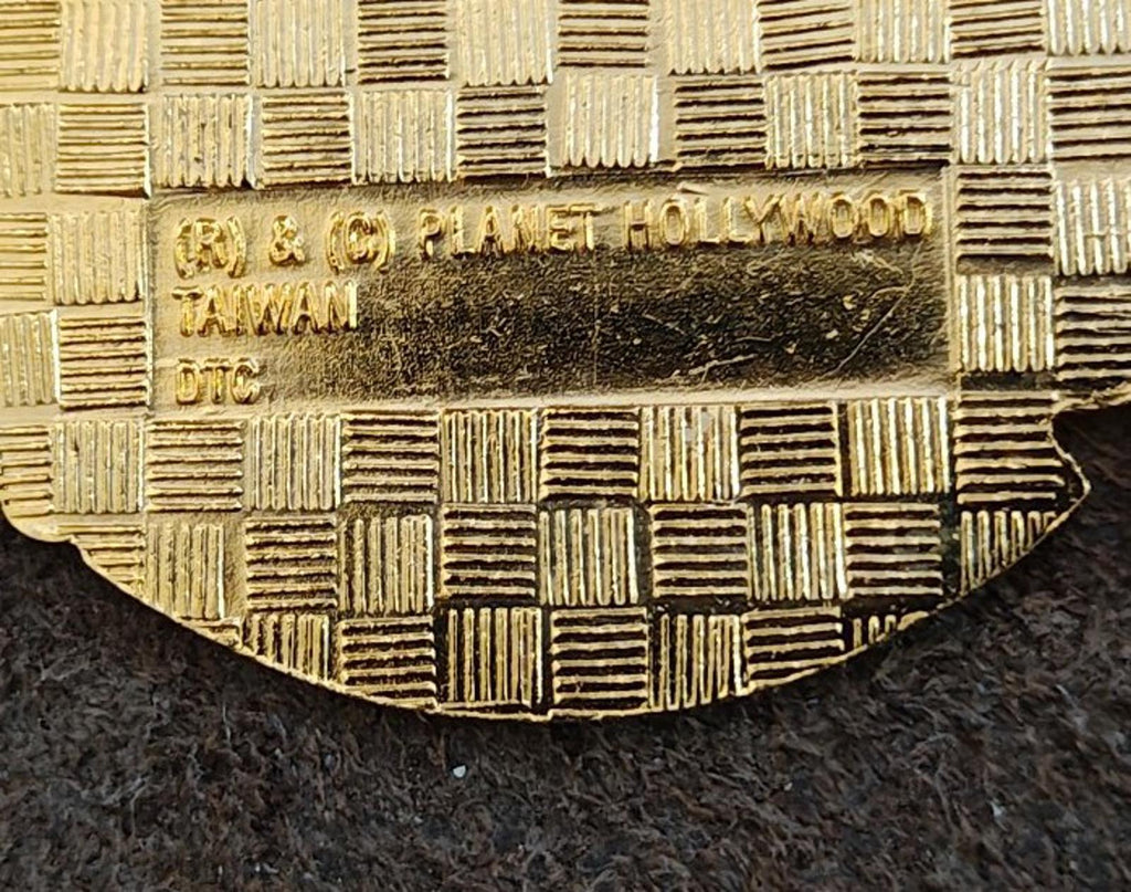 Gold-tone enamel pin back close-up with stamped lettering and checkered texture