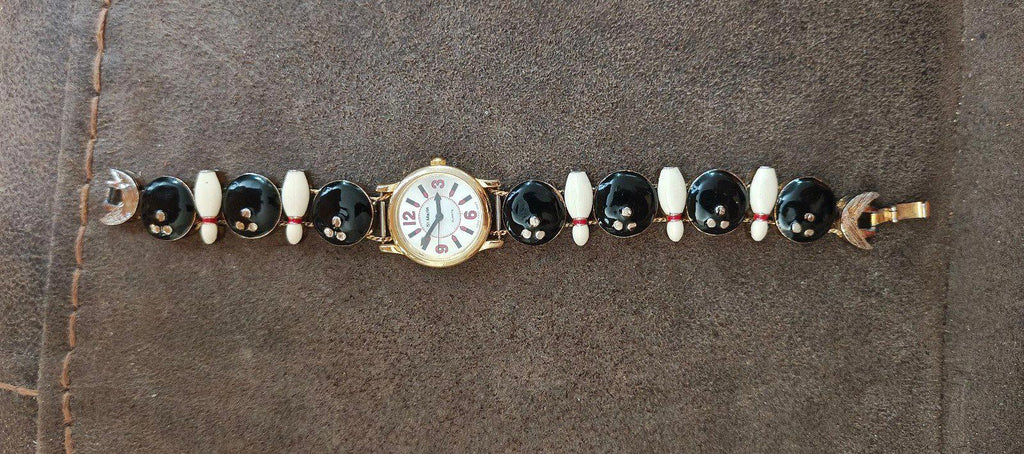 Novelty ladies watch bracelet laid flat: gold-tone case centered with black and white link charms
