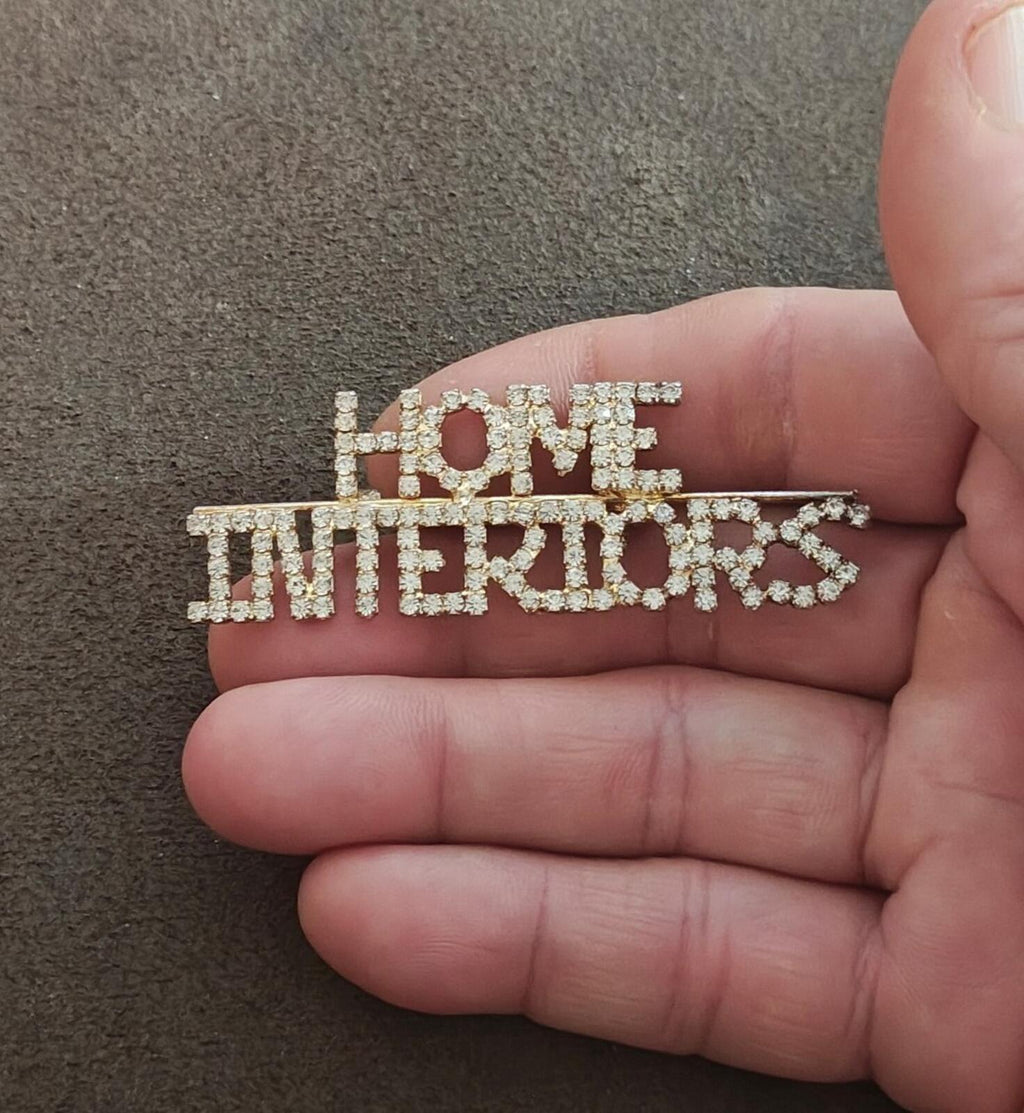 Gold-tone rhinestone brooch reading "HOME INTERIORS" with red heart accent