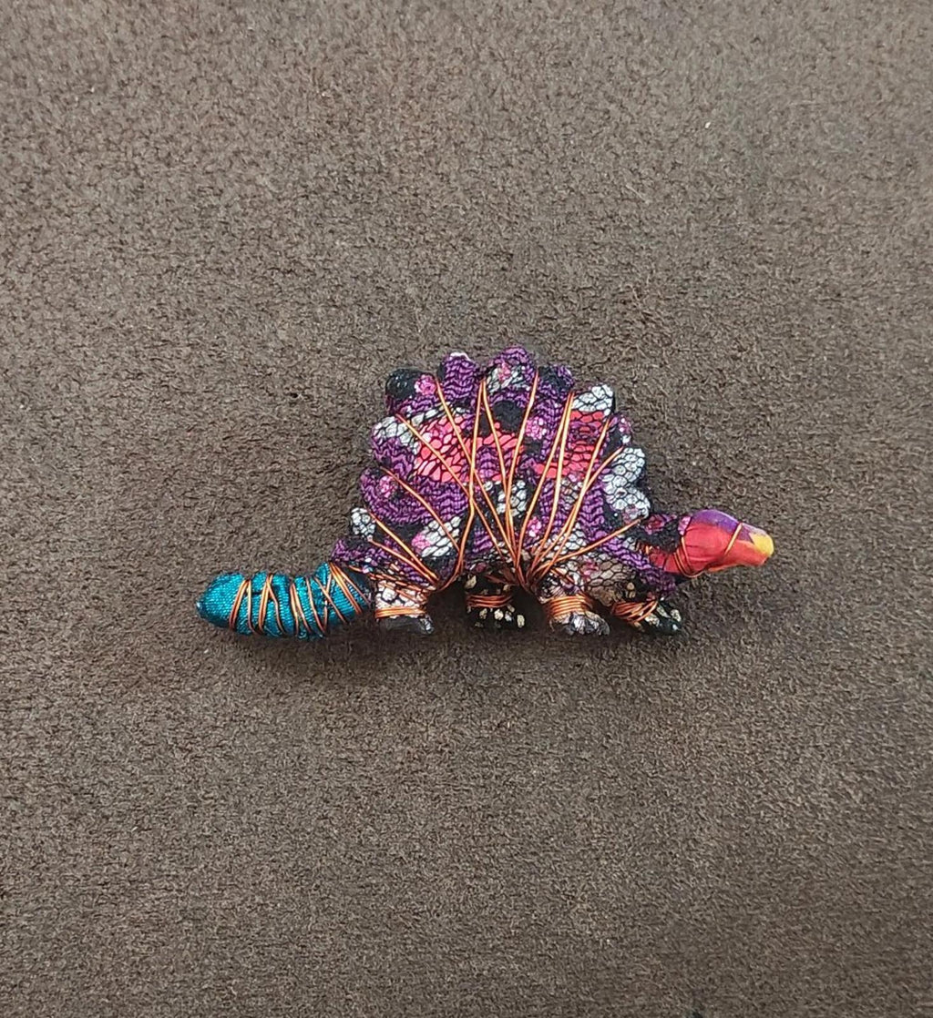 Purple stegosaurus dinosaur brooch lying flat, rhinestone mosaic body with turquoise tail